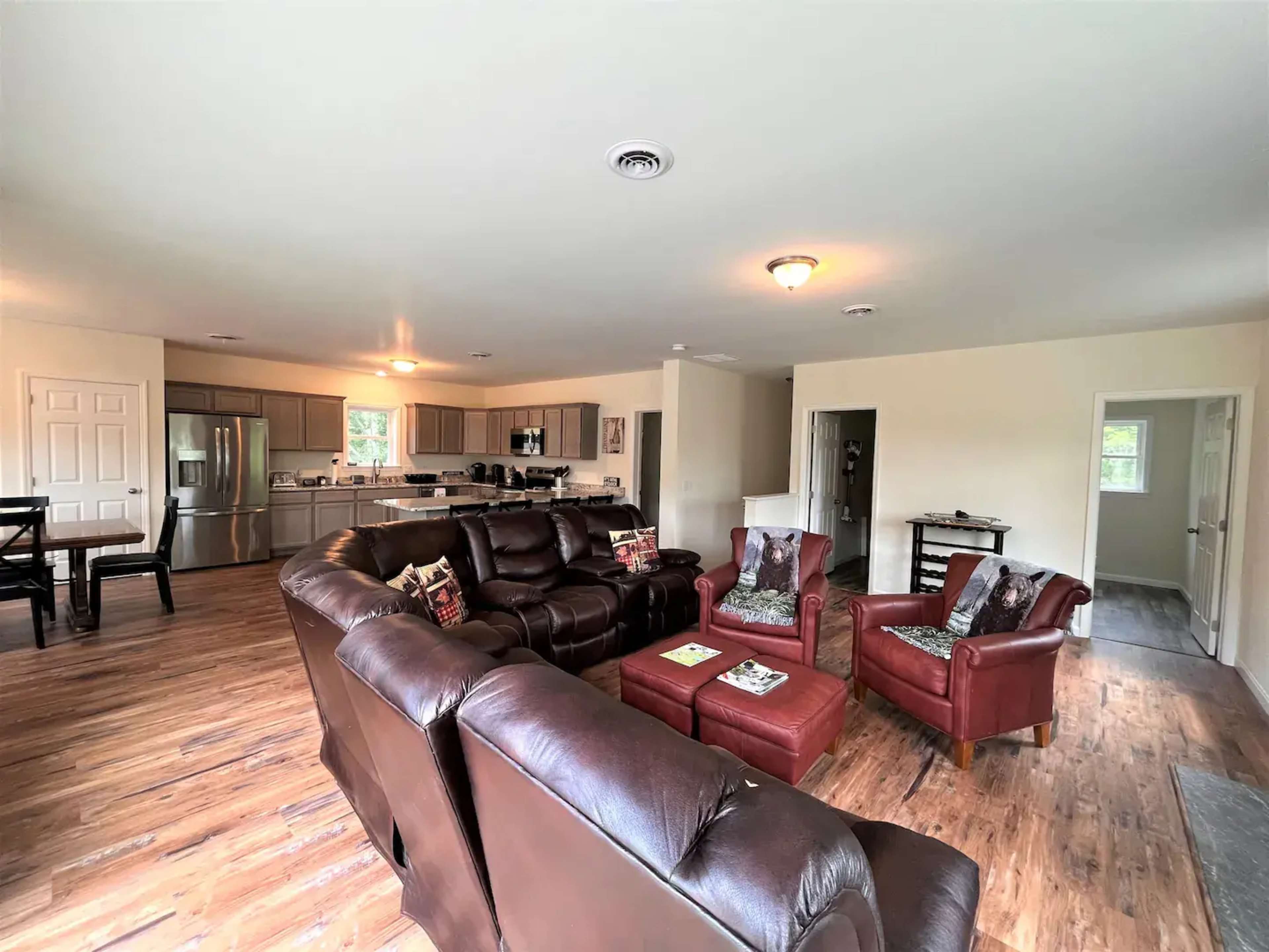 A spacious living area with brown leather sofas, armchairs, and an open kitchen in the background.