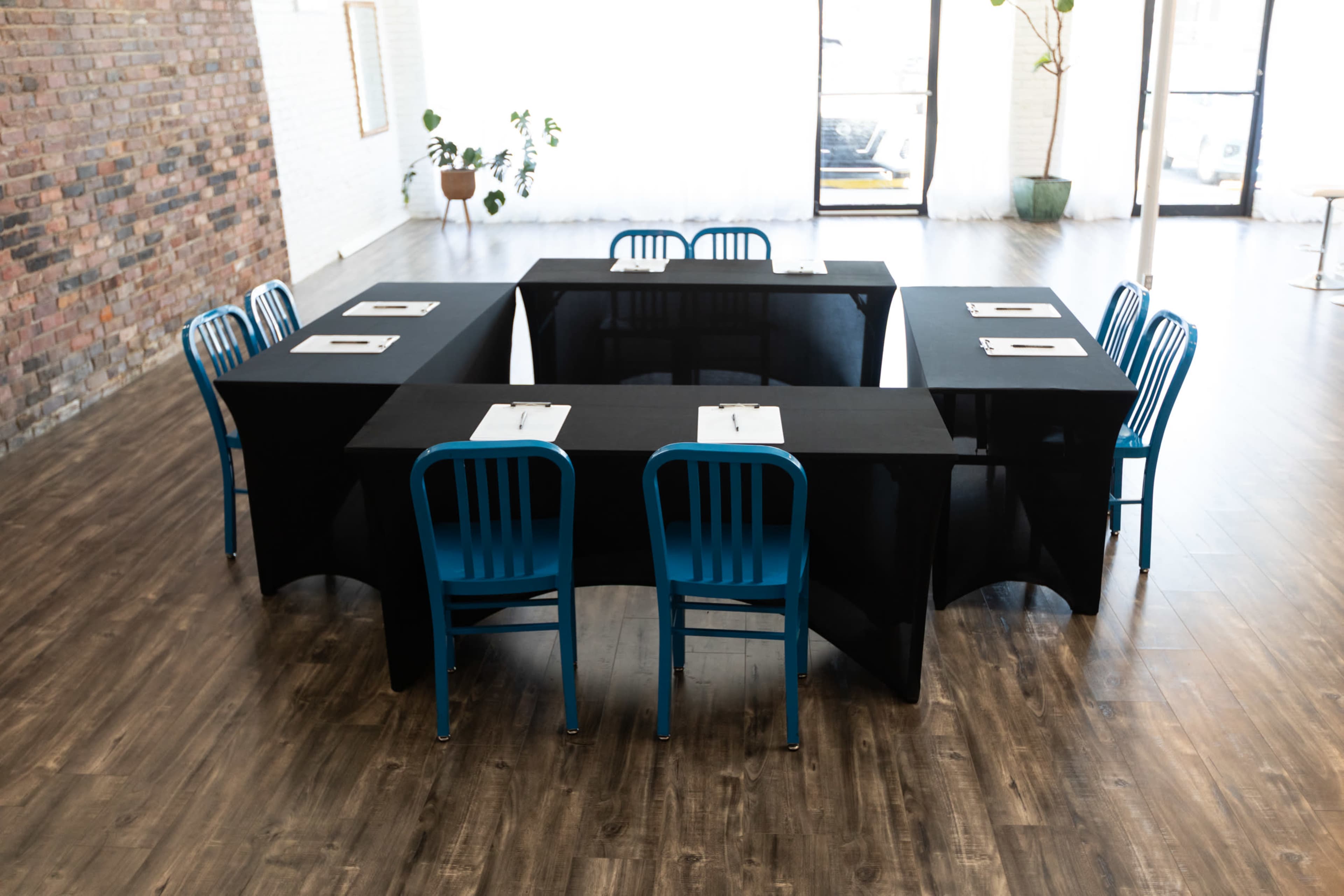 The image shows a rectangular arrangement of black tables with blue chairs positioned around them in a spacious, well-lit room.