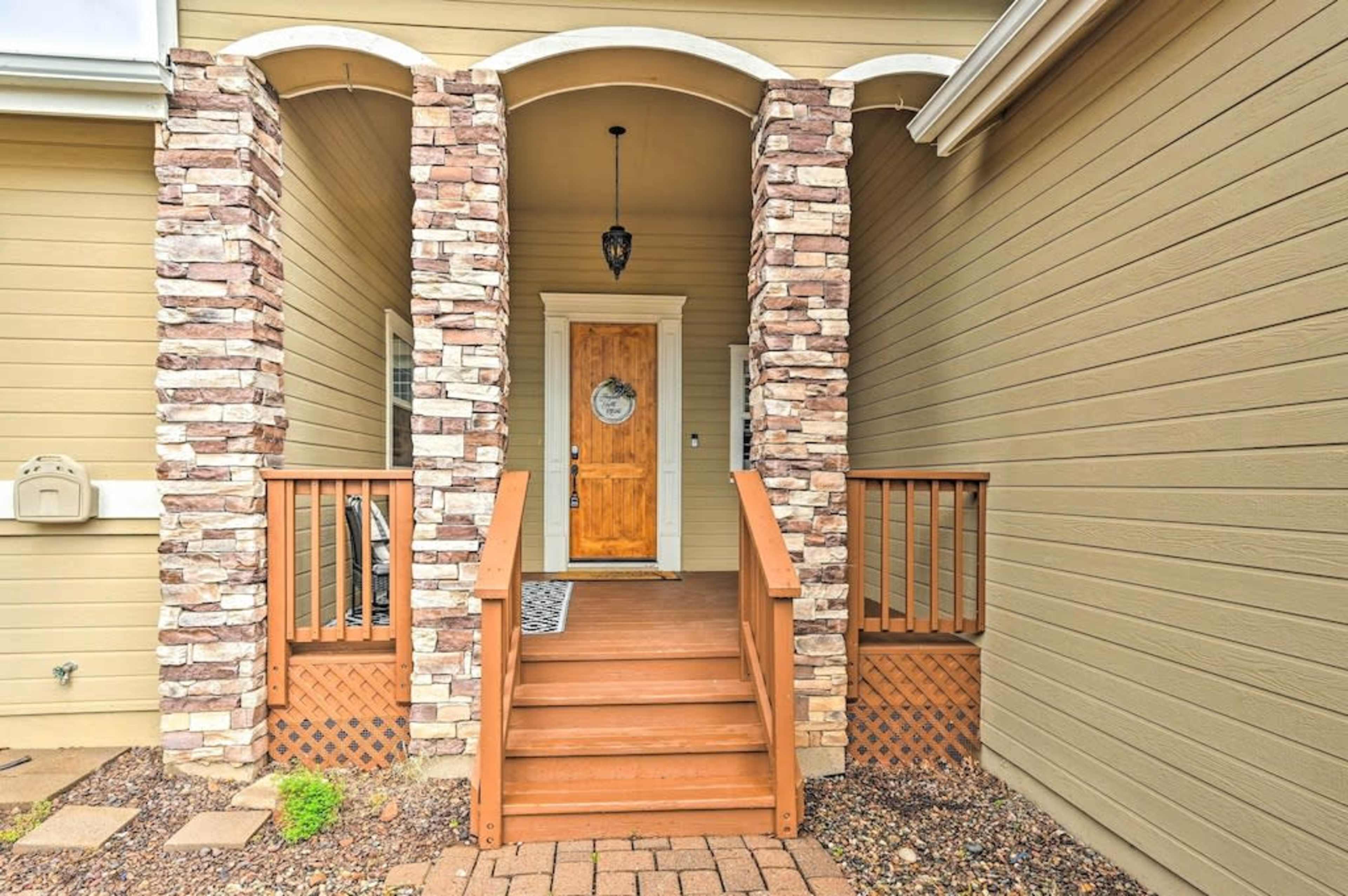 The entryway features wooden steps leading to a front door framed by stone columns and a light fixture above.