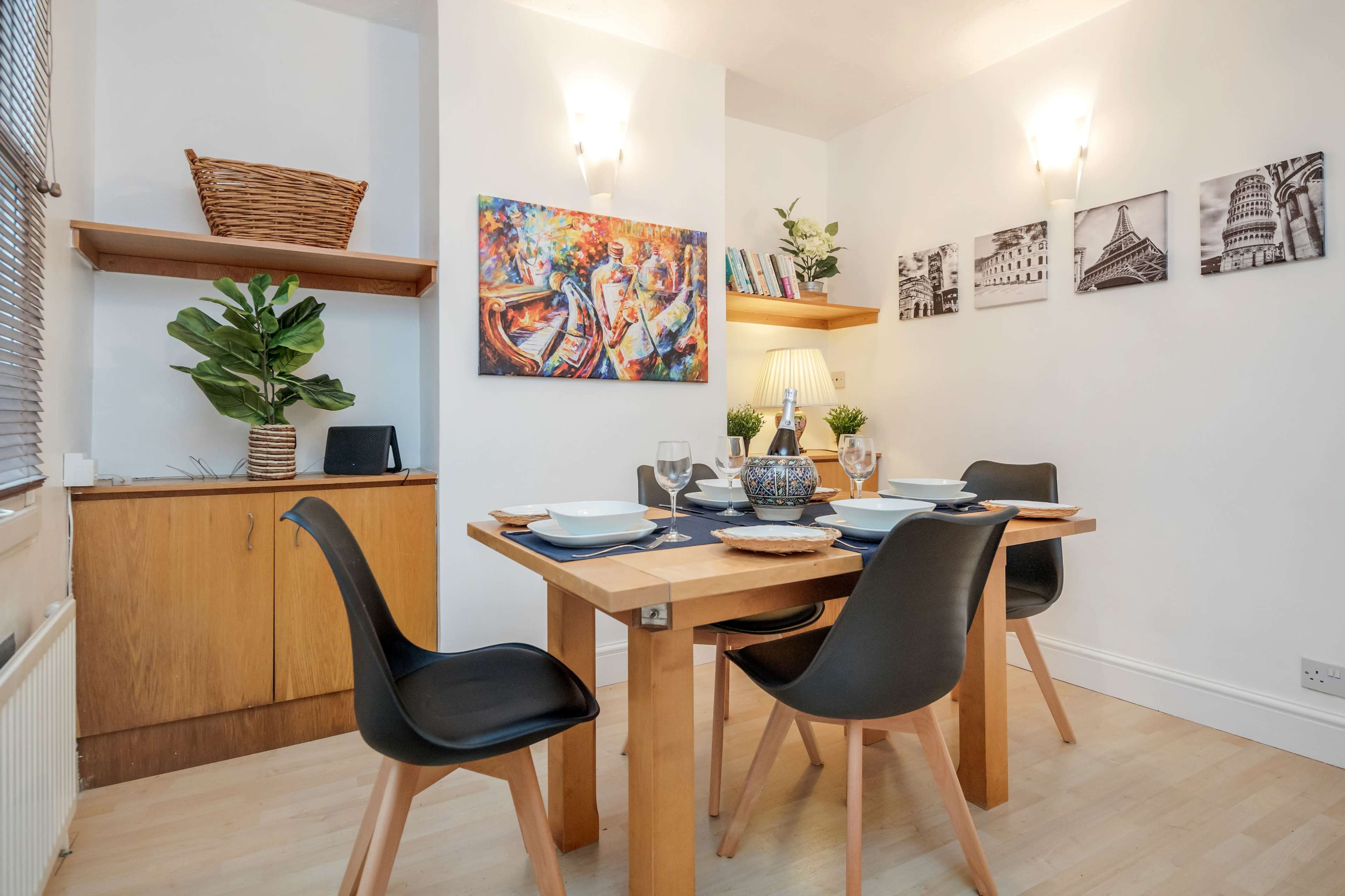 A dining area with a wooden table set for four, surrounded by black chairs, and decorated with wall art and indoor plants.