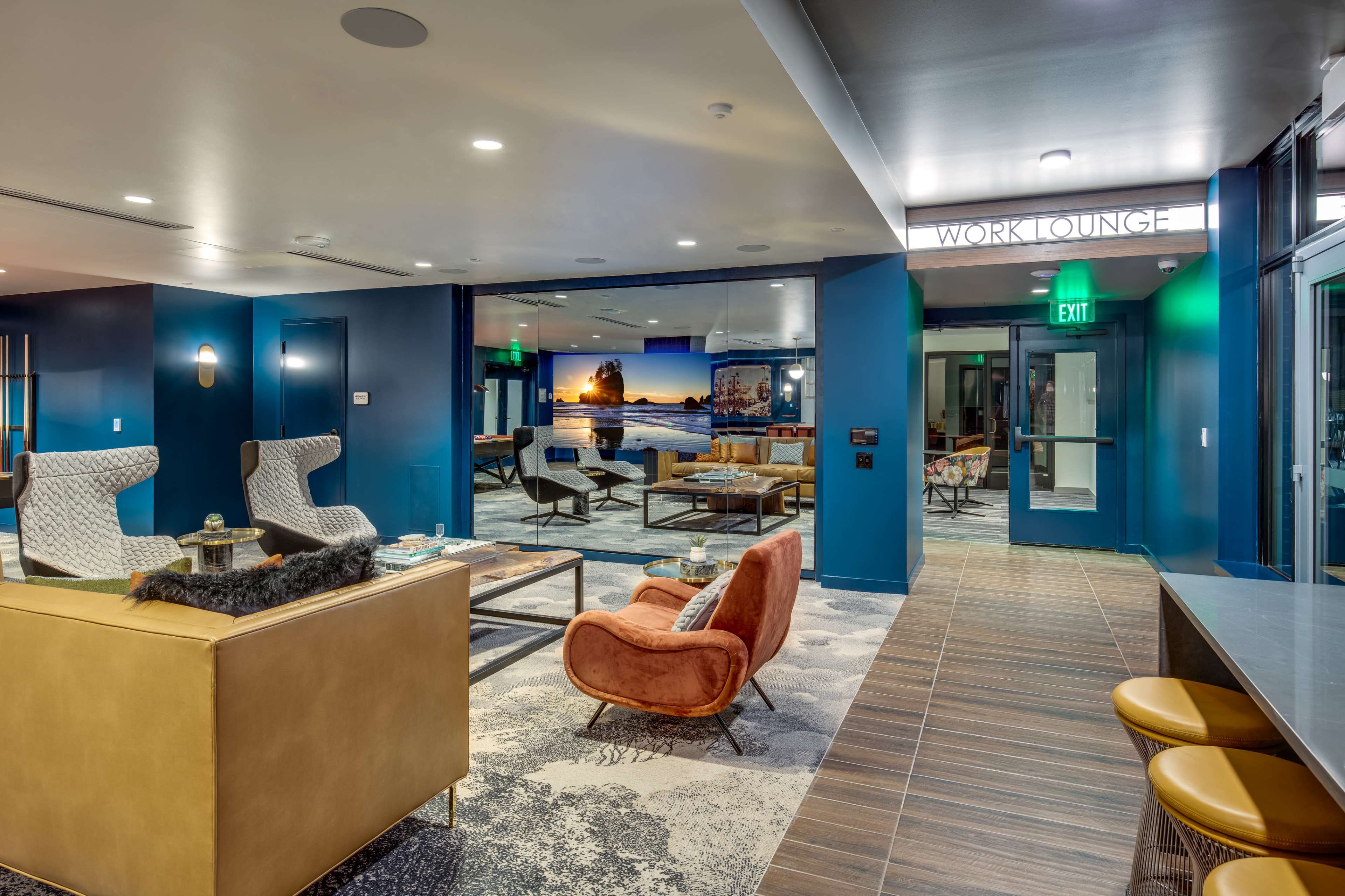 A modern work lounge featuring cozy seating, workstations, and blue walls, designed for collaboration and relaxation.