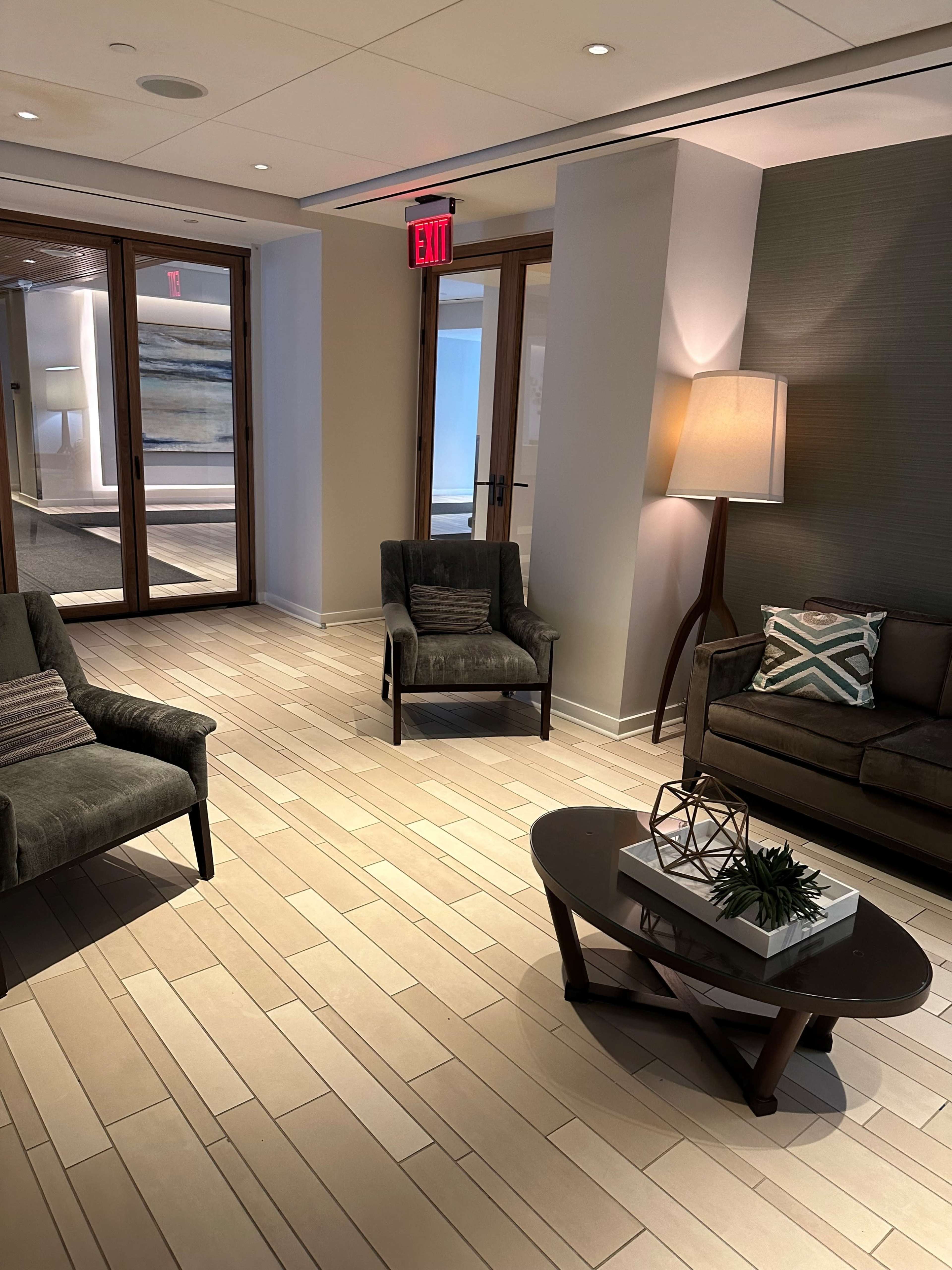 The image shows a modern lounge area with two armchairs, a sofa, and a coffee table on a plank floor, with large glass doors leading to another room.