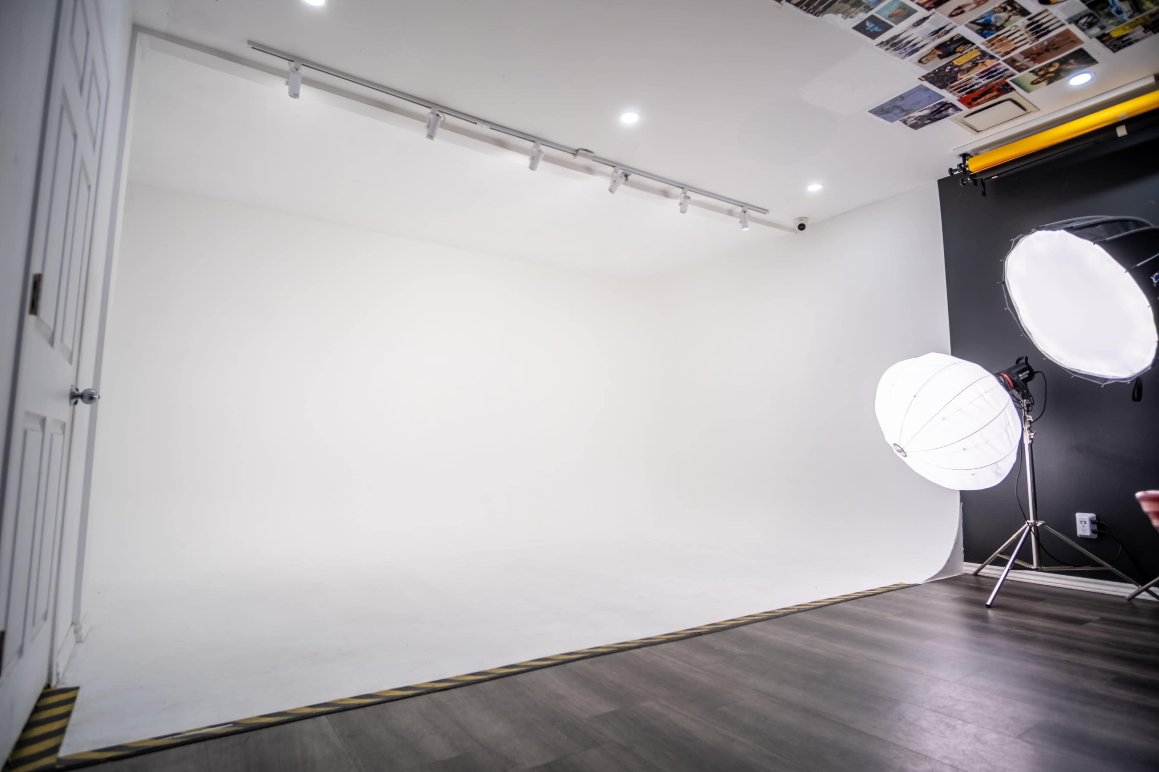The image shows a blank photography studio space with a white backdrop, lighting equipment, and a door on one side.