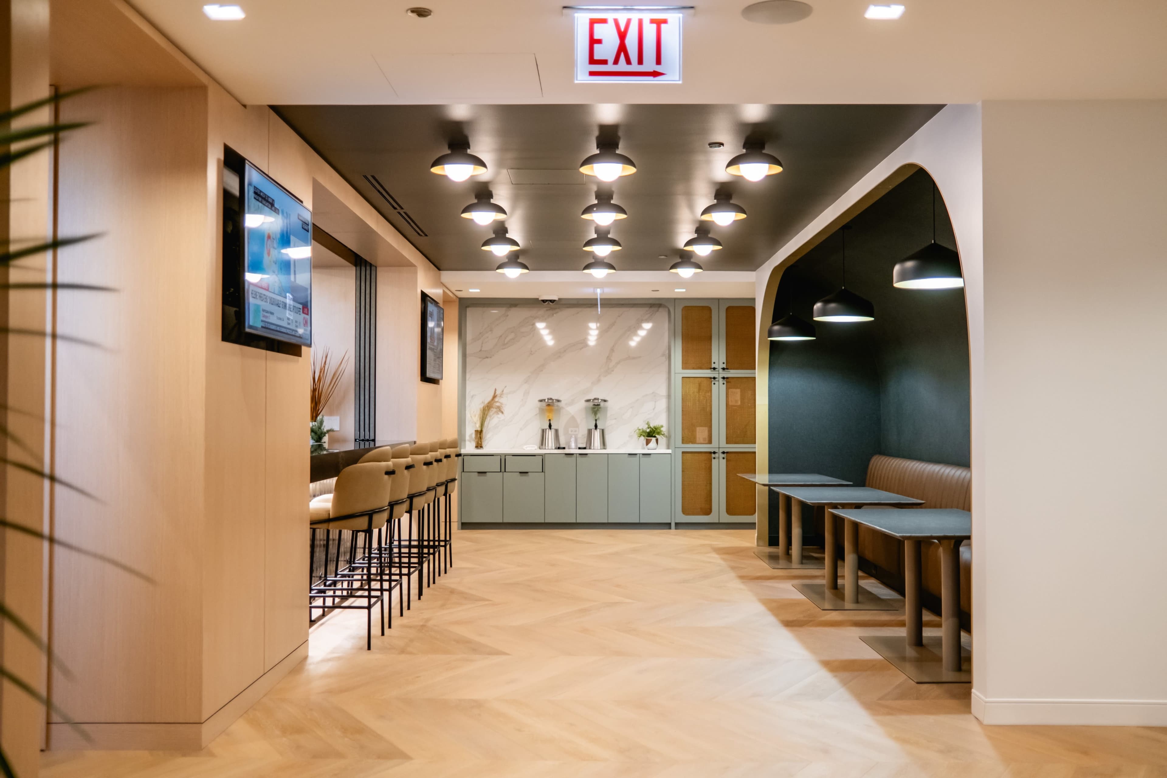The image shows a modern interior design of an office space featuring a seating area with bar stools, tables, and stylish lighting fixtures.