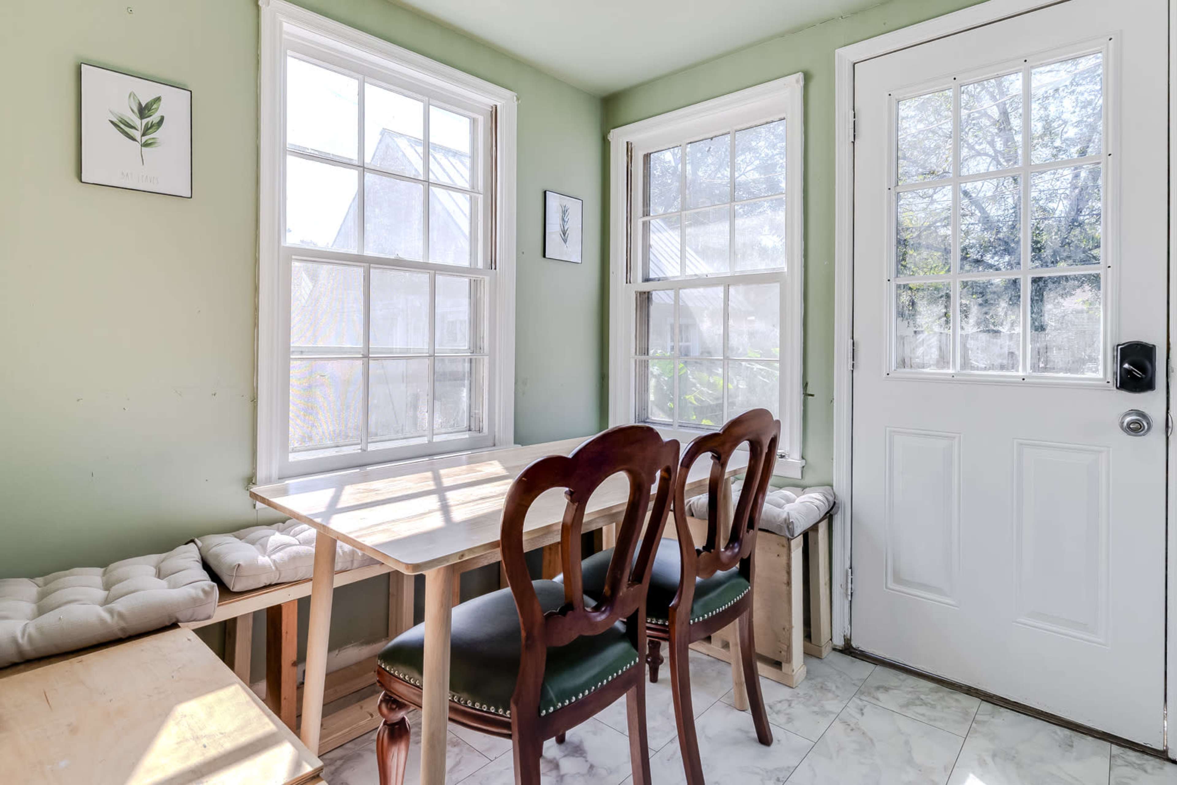A small dining area features a wooden table and two chairs near a door with large windows allowing natural light to enter.