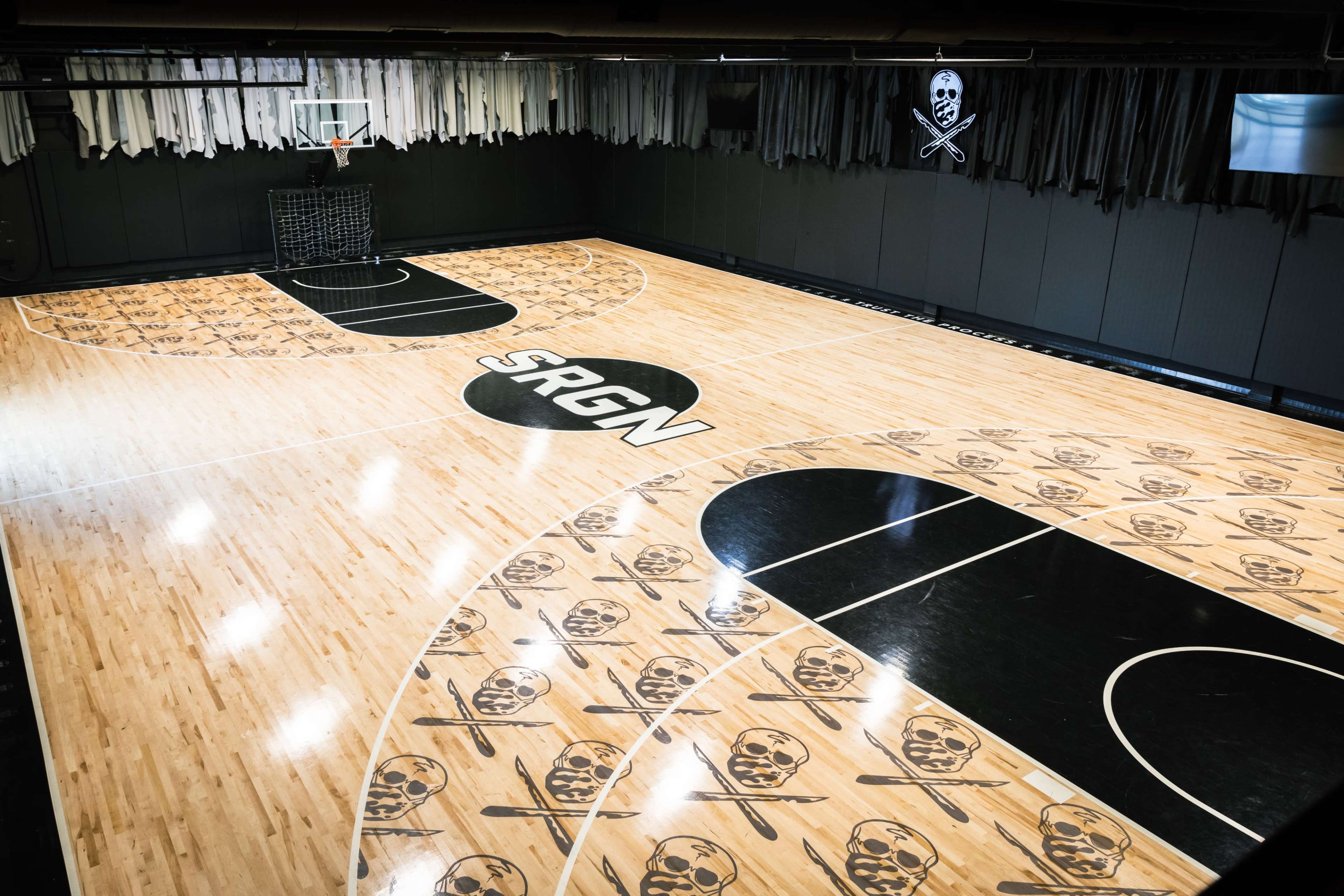 The image shows a basketball court featuring a wooden floor with skull and crossbones designs and the letters "SRGN" prominently displayed at the center.