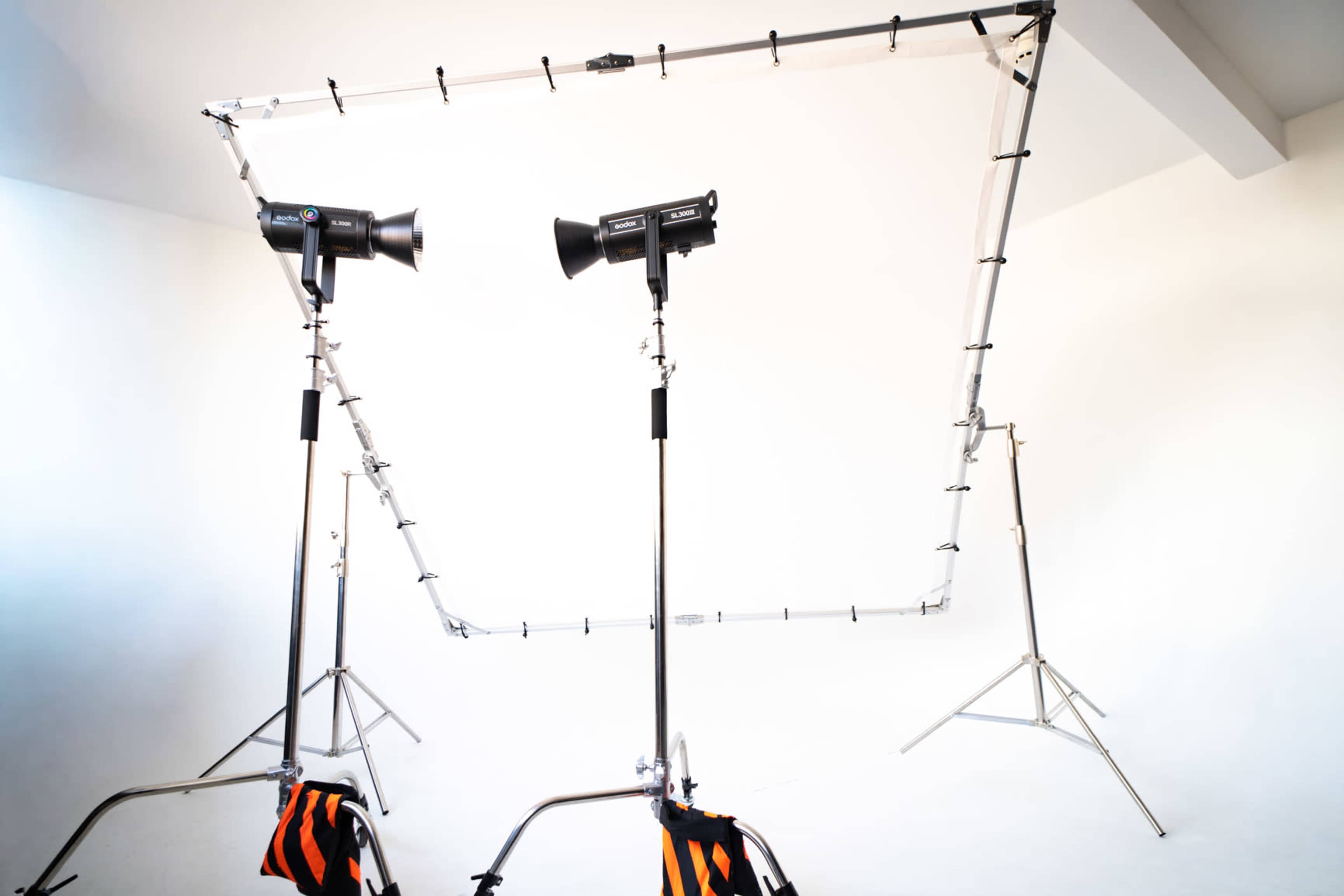 The image shows a photography setup with two lighting fixtures mounted on stands and a backdrop support frame positioned in a white studio space.