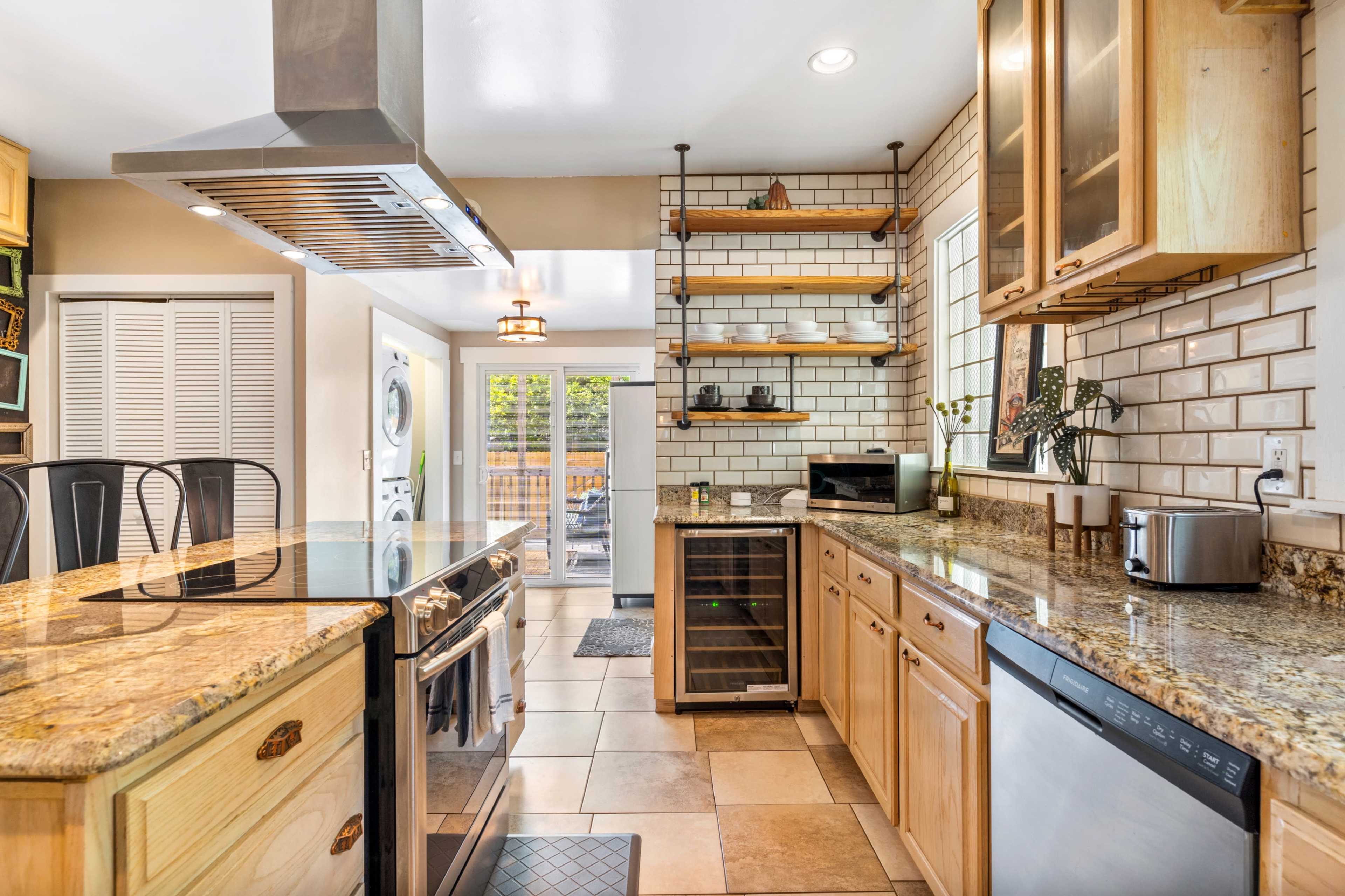 A modern kitchen with wooden cabinets, granite countertops, and stainless steel appliances, featuring an open layout with a view into an outdoor space.