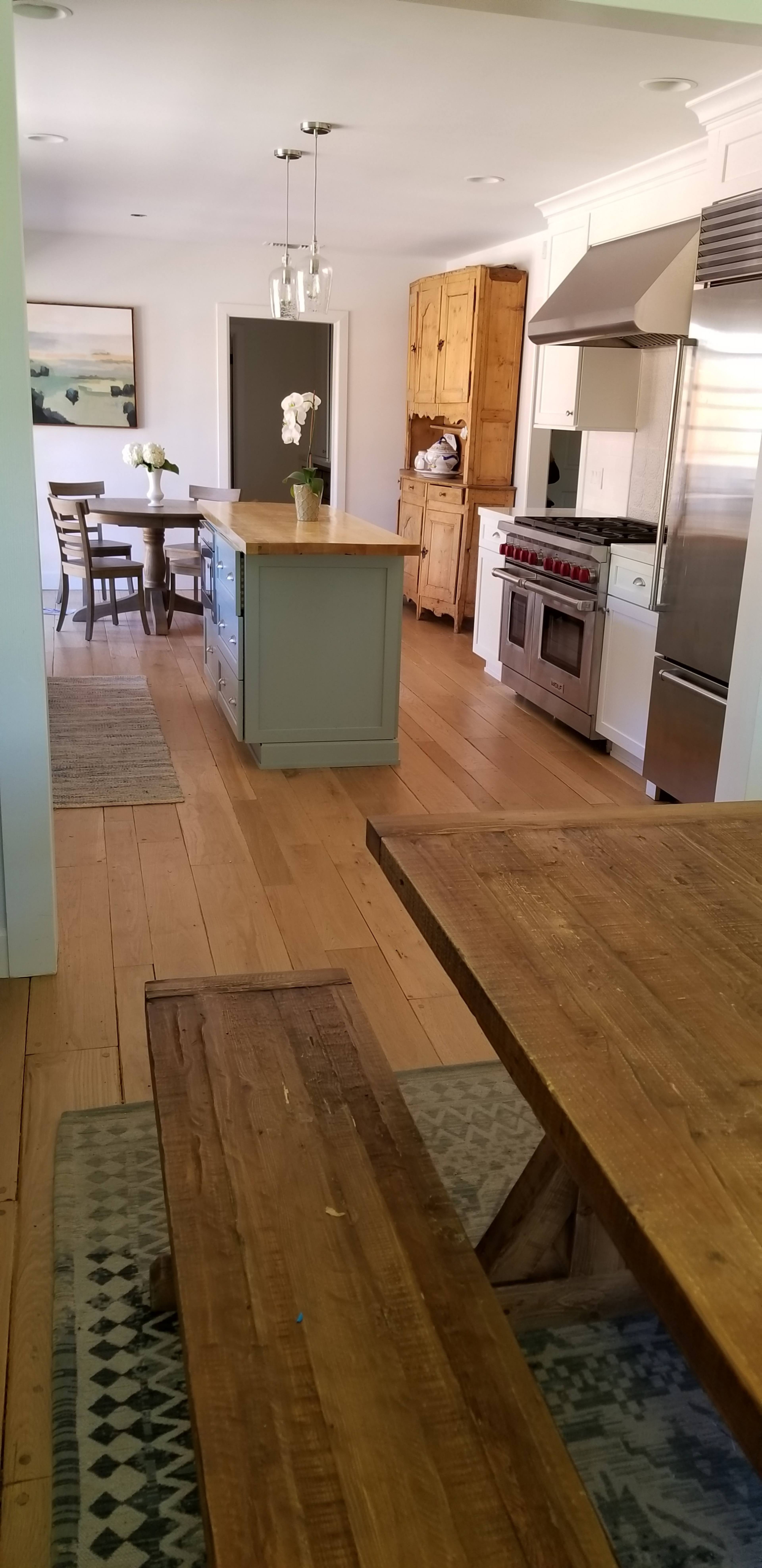 A kitchen with a central island, stainless steel appliances, a dining table, and wooden flooring.