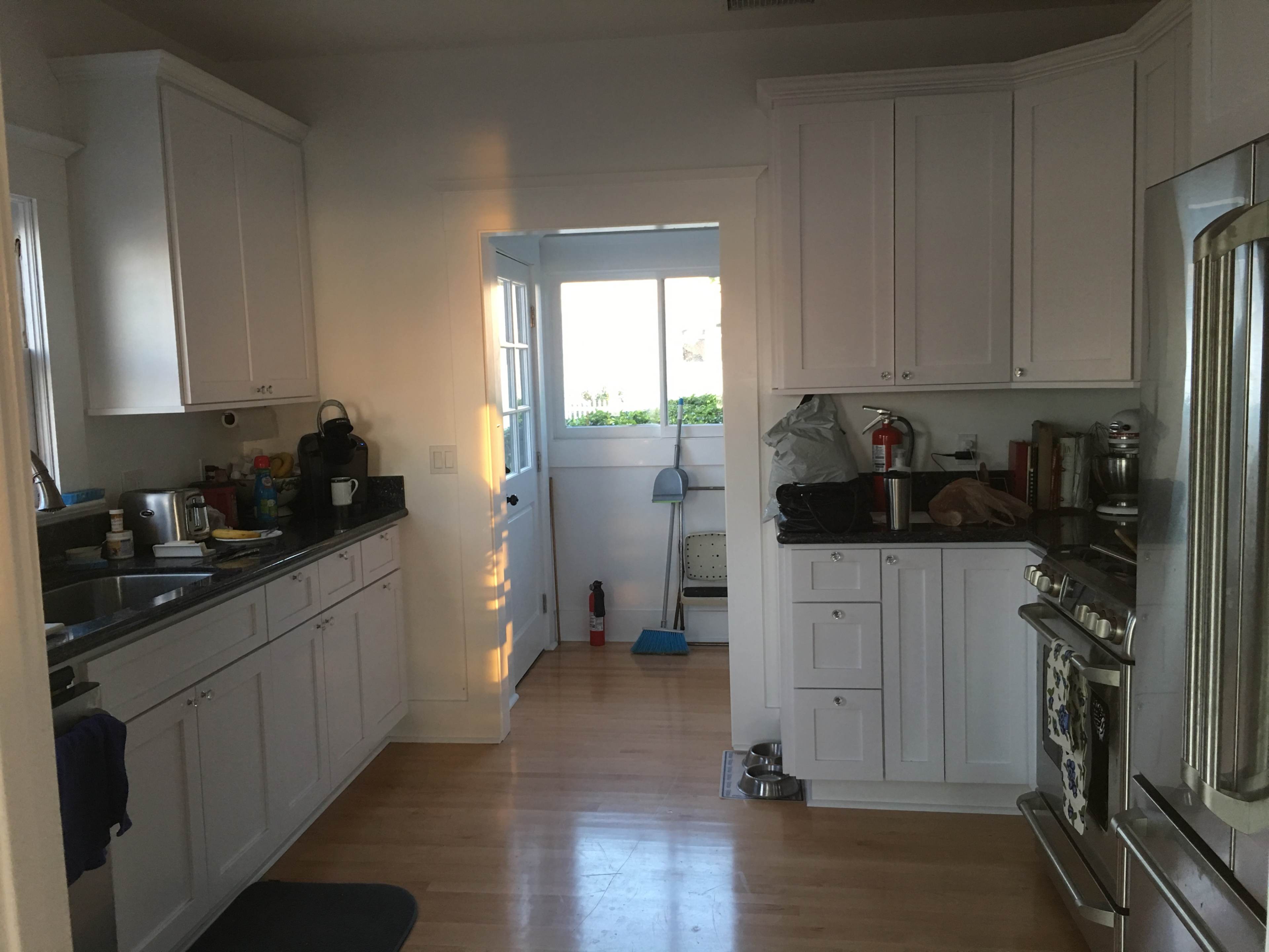 A kitchen with white cabinets, a stainless steel stove, and an adjacent doorway leading to a bright area.