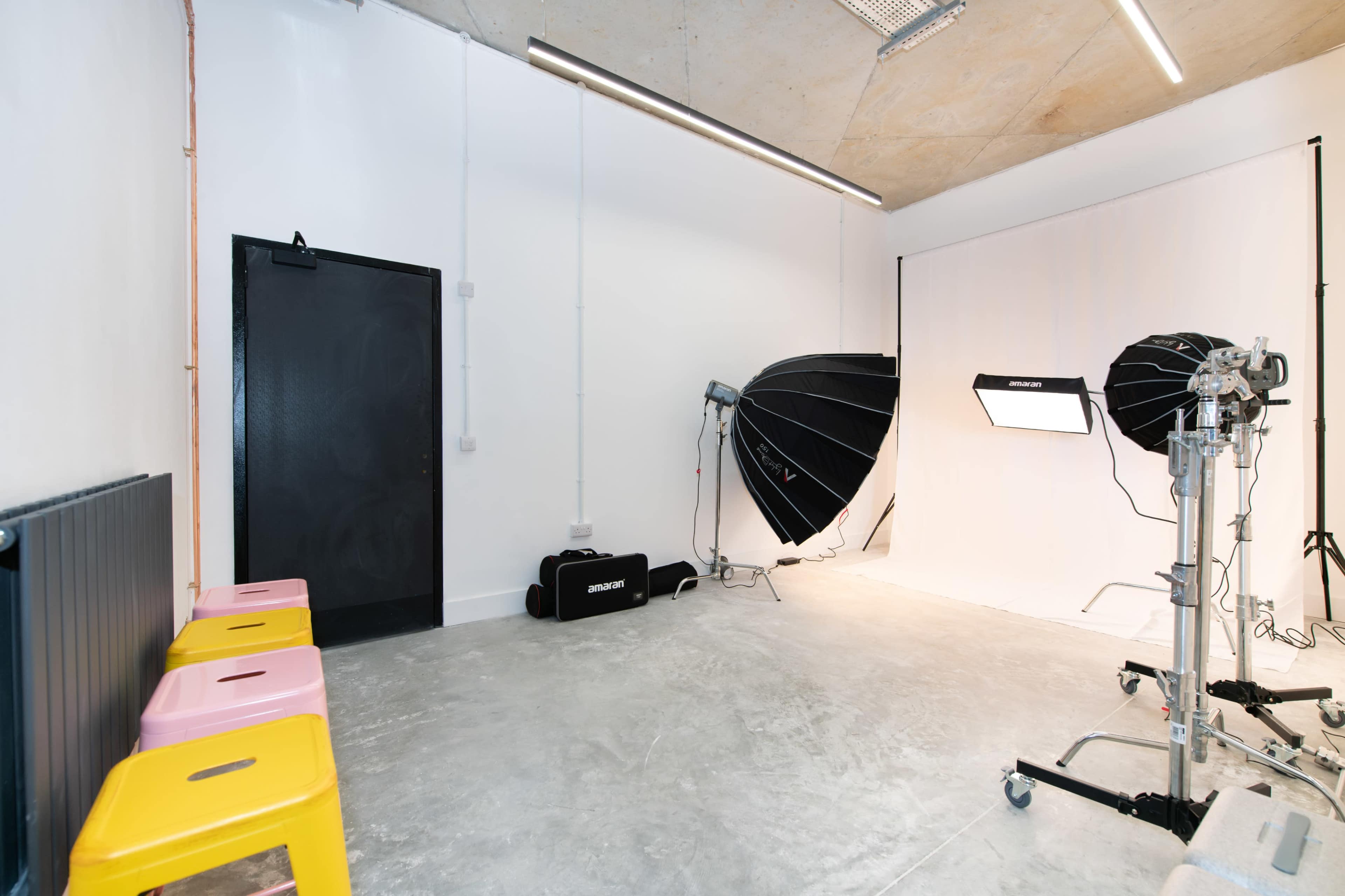 A photography studio with two large softbox lights, a plain white backdrop, and colorful stools arranged in front of the setup.