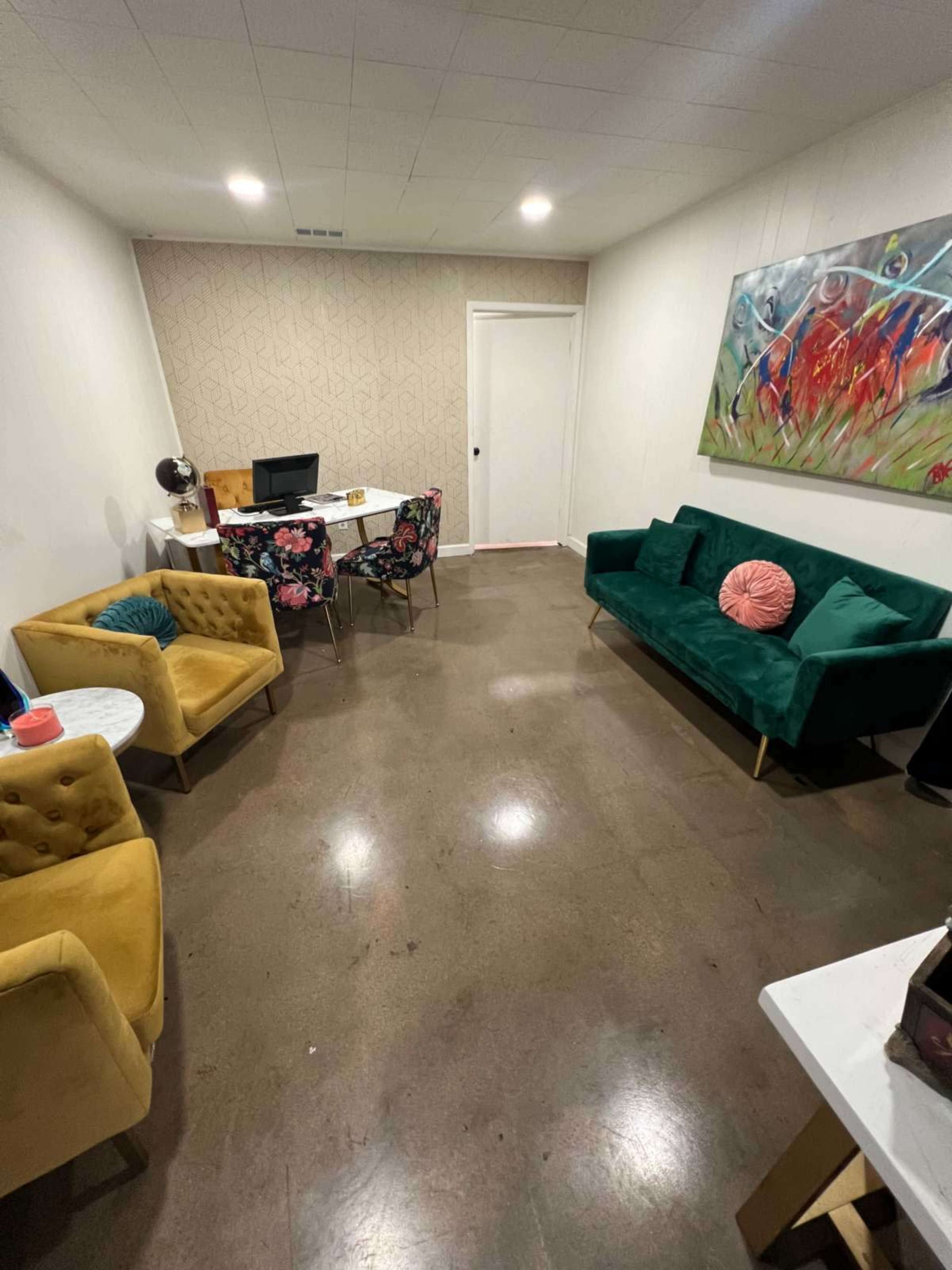The image shows a modern office space with a desk, computer, and seating areas featuring colorful chairs and a floral-patterned tablecloth.