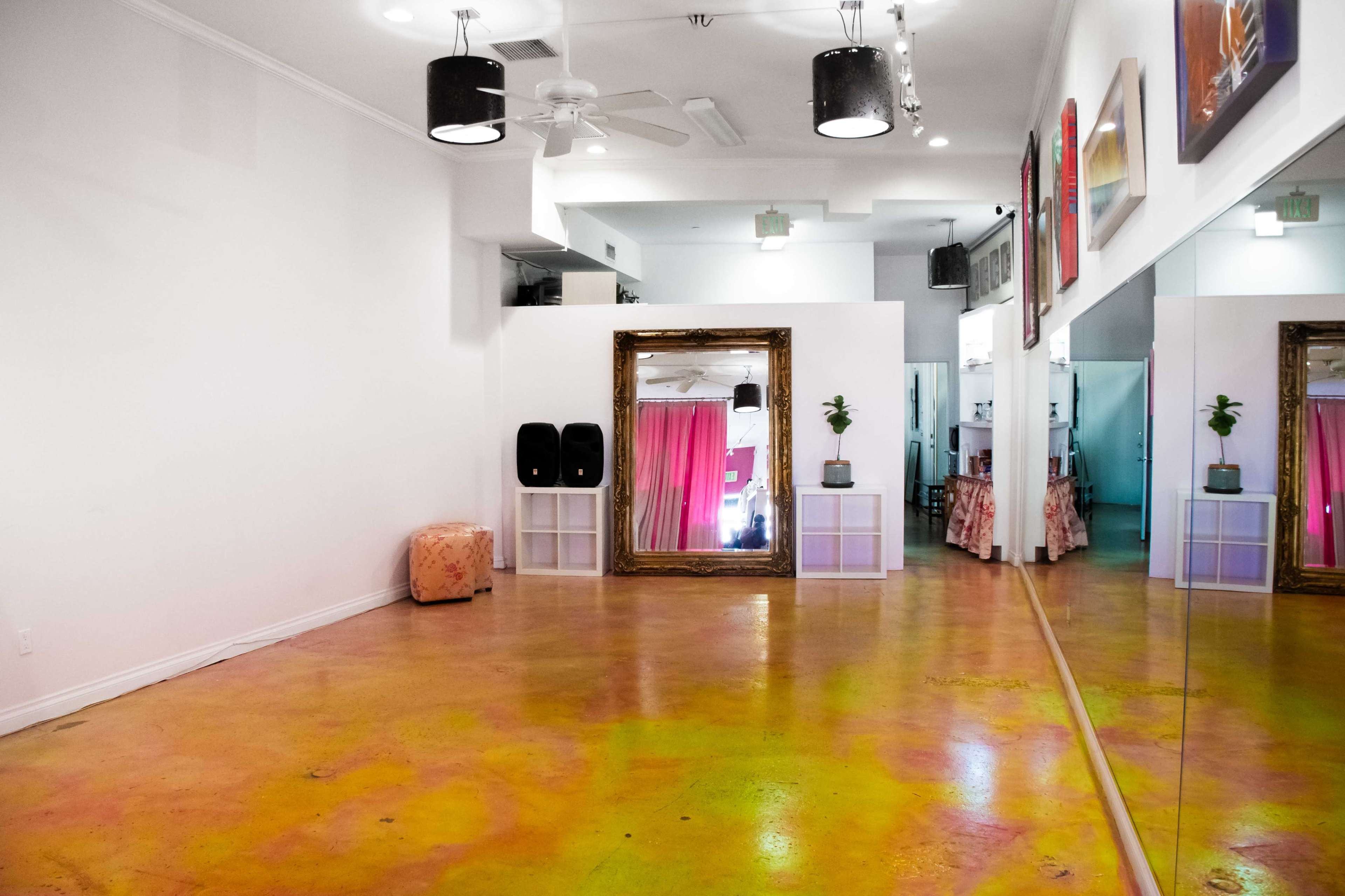 The image shows an empty studio space featuring a large mirror, a gold-framed mirror, and a polished floor with colorful patterns.