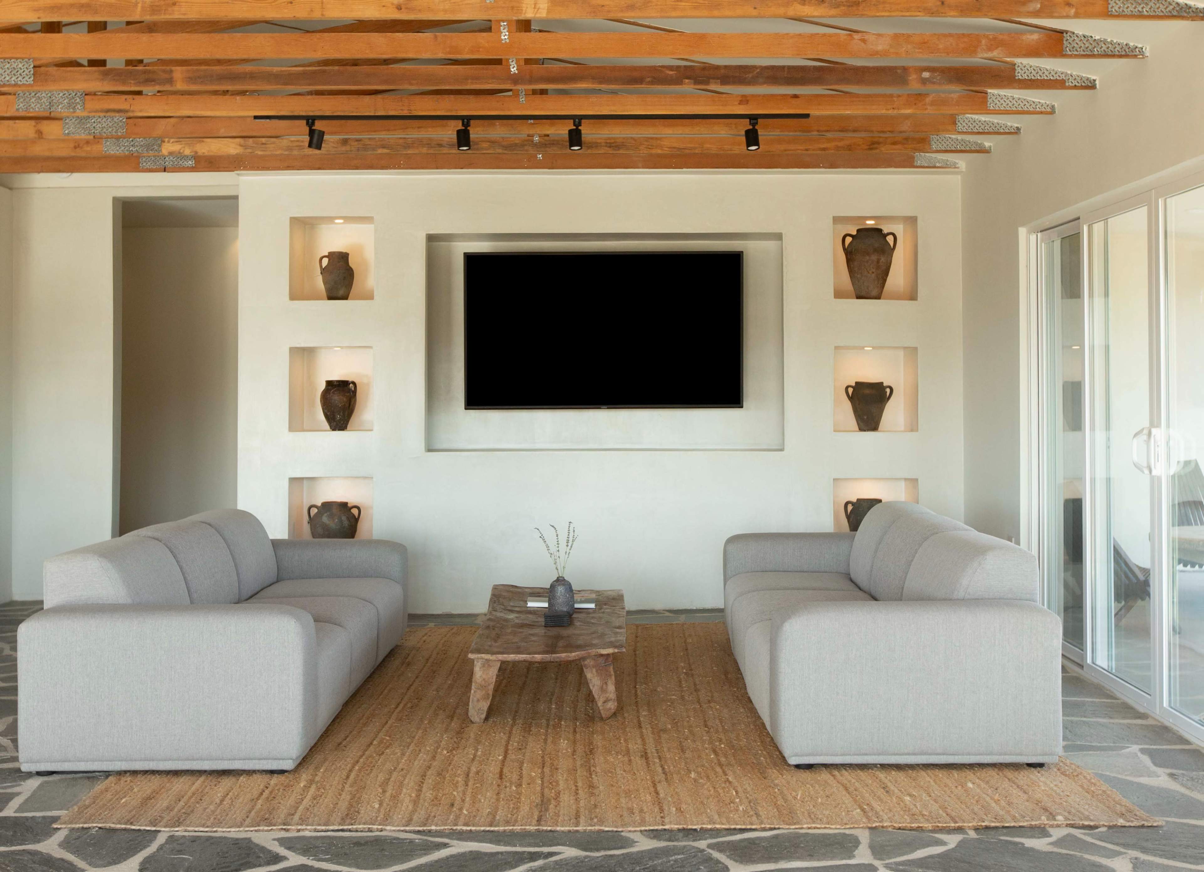 The image shows a modern living room with two gray couches facing a wooden coffee table on a textured stone floor, set against a wall featuring built-in shelves with decorative vases.
