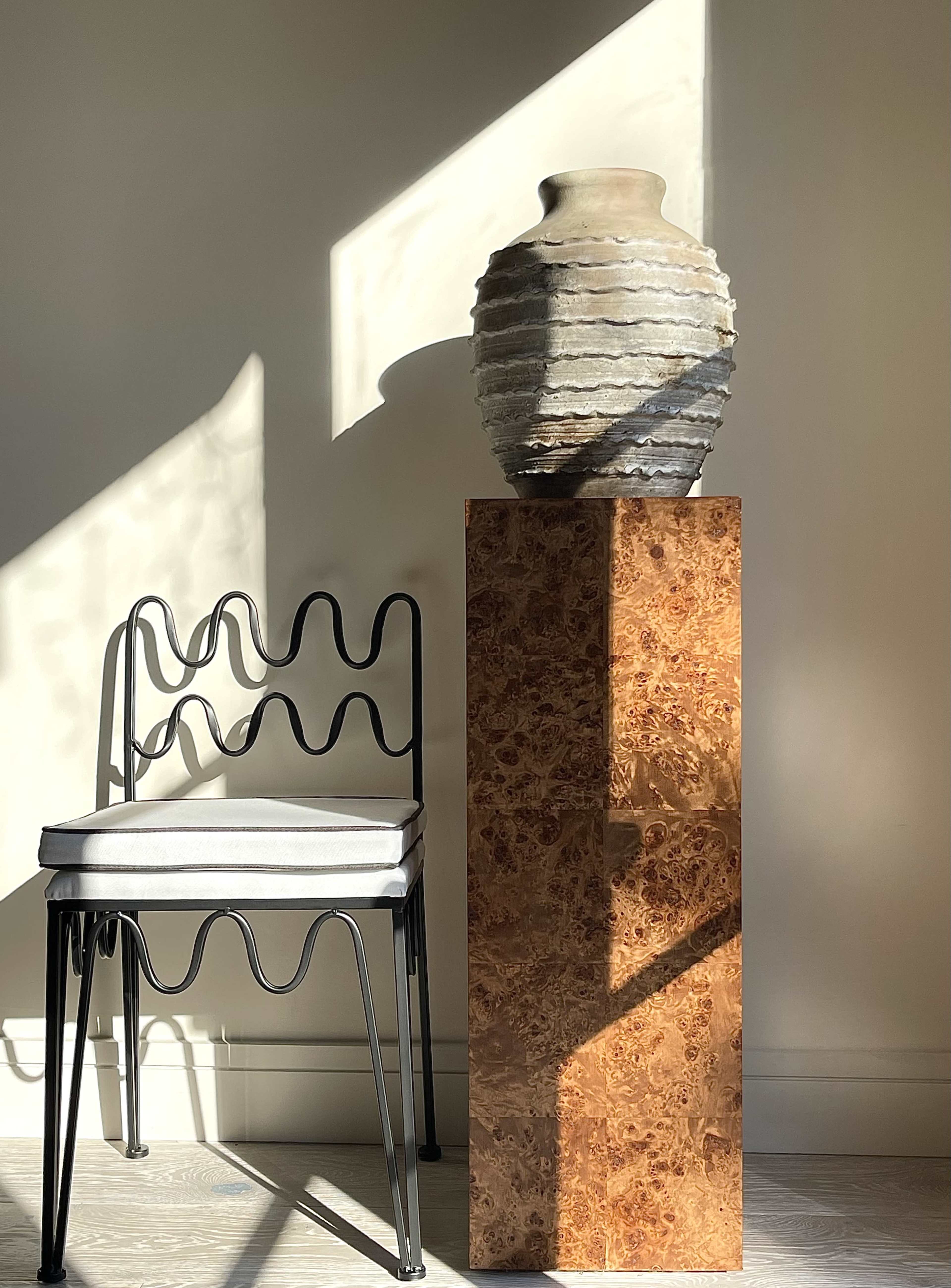 A decorative vase sits atop a textured pedestal beside a modern chair with a wavy design.