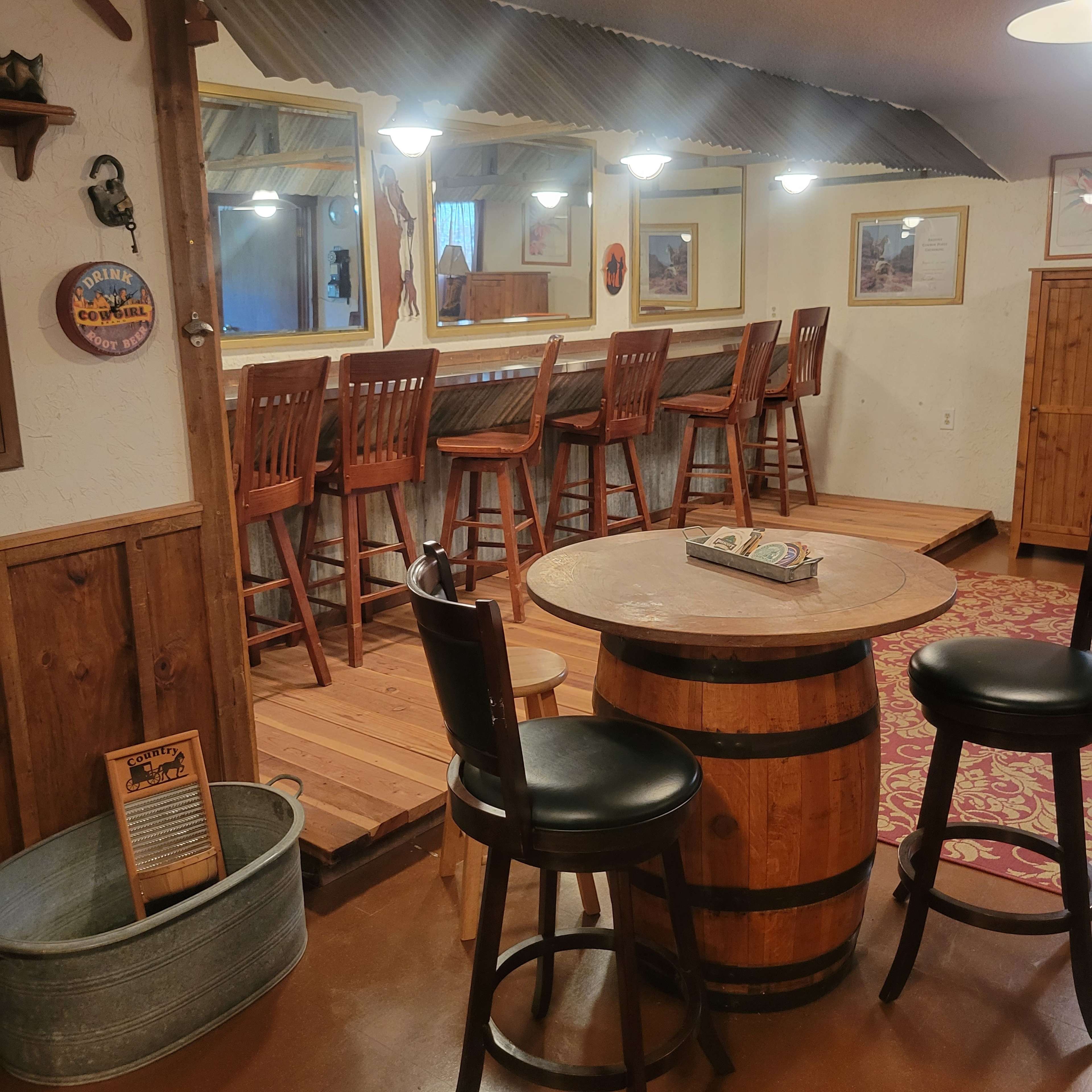 The image shows a rustic interior with wooden bar stools and tables, featuring a bar area with a mirrored wall and a decorative theme.