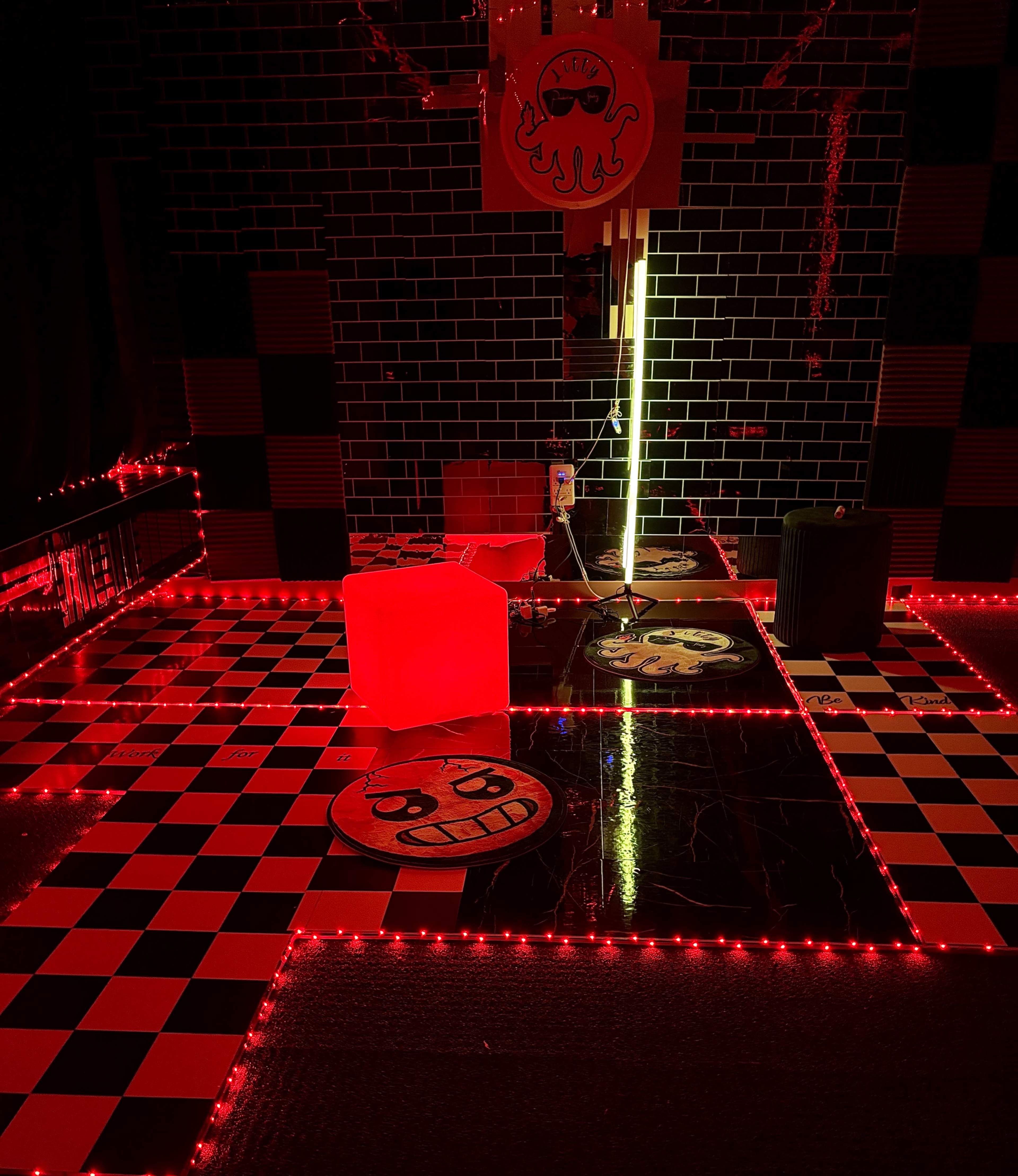 The image shows a room with a black and red checkerboard floor illuminated by red LED lights, featuring a large octopus decoration and various playful floor designs.