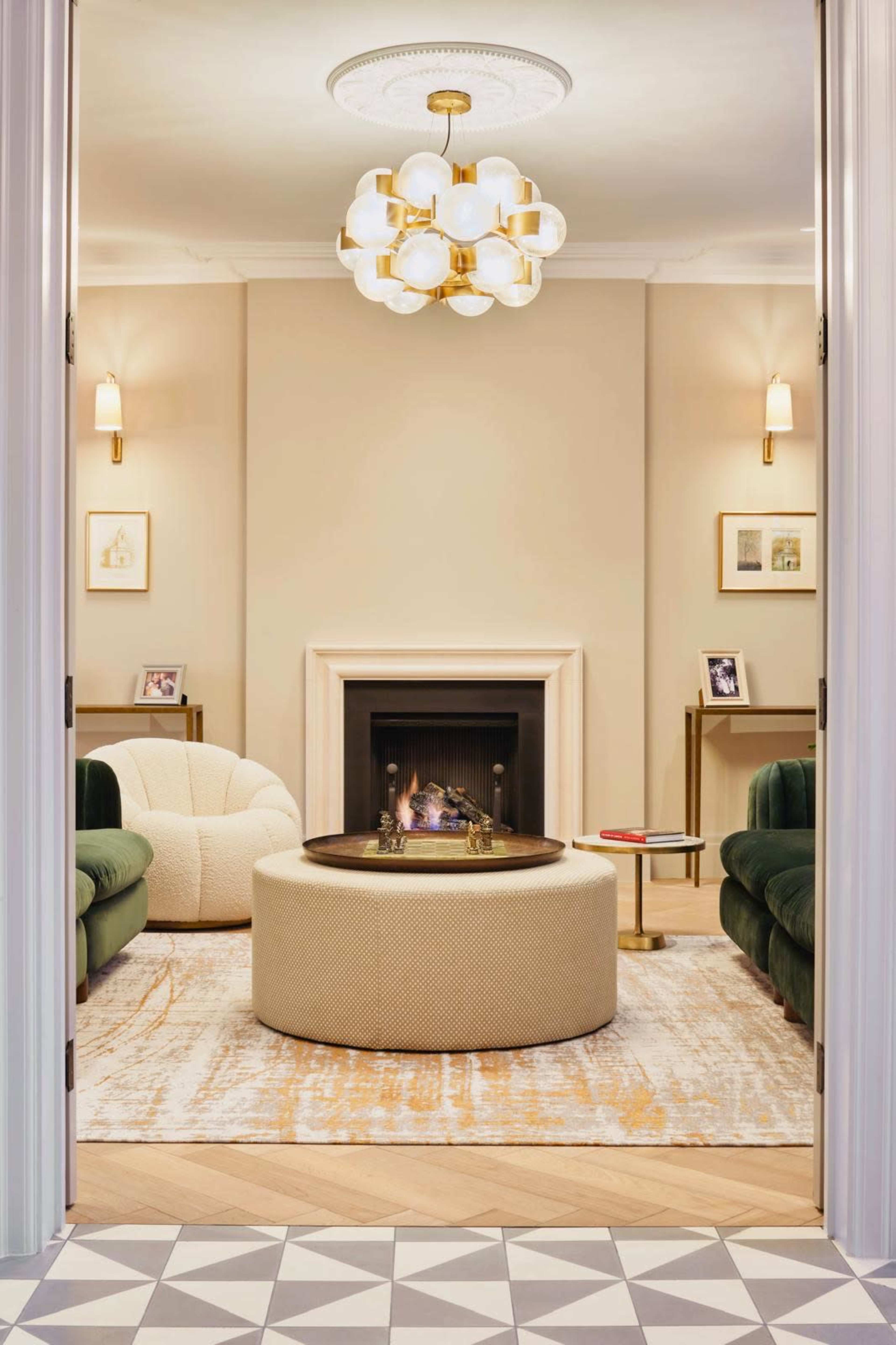 The image depicts a stylish living room featuring a round coffee table, two green sofas, a fireplace, and elegant lighting fixtures.