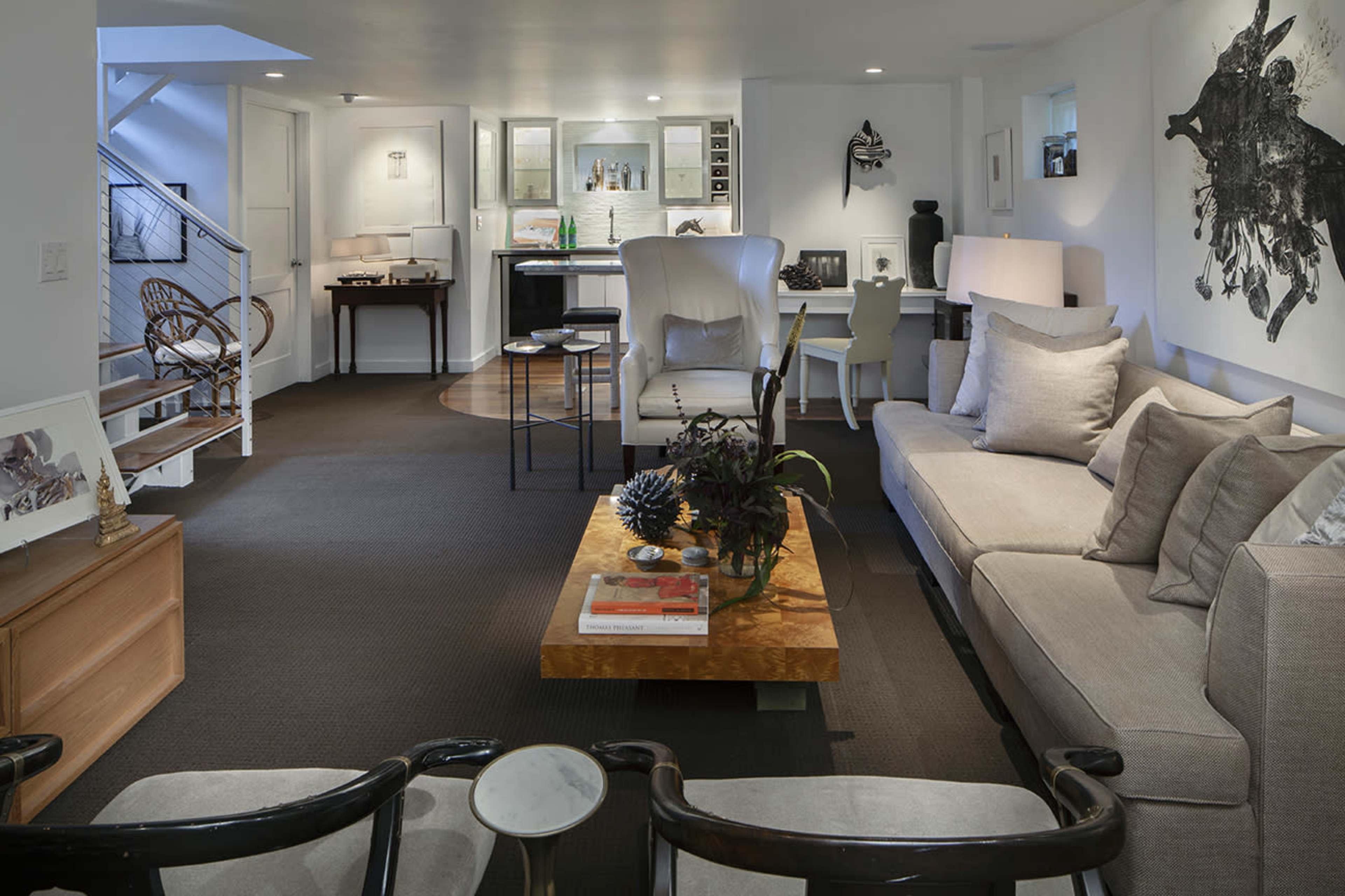 The image shows a modern living room with a beige sofa, a wooden coffee table, and various seating areas under bright lighting.