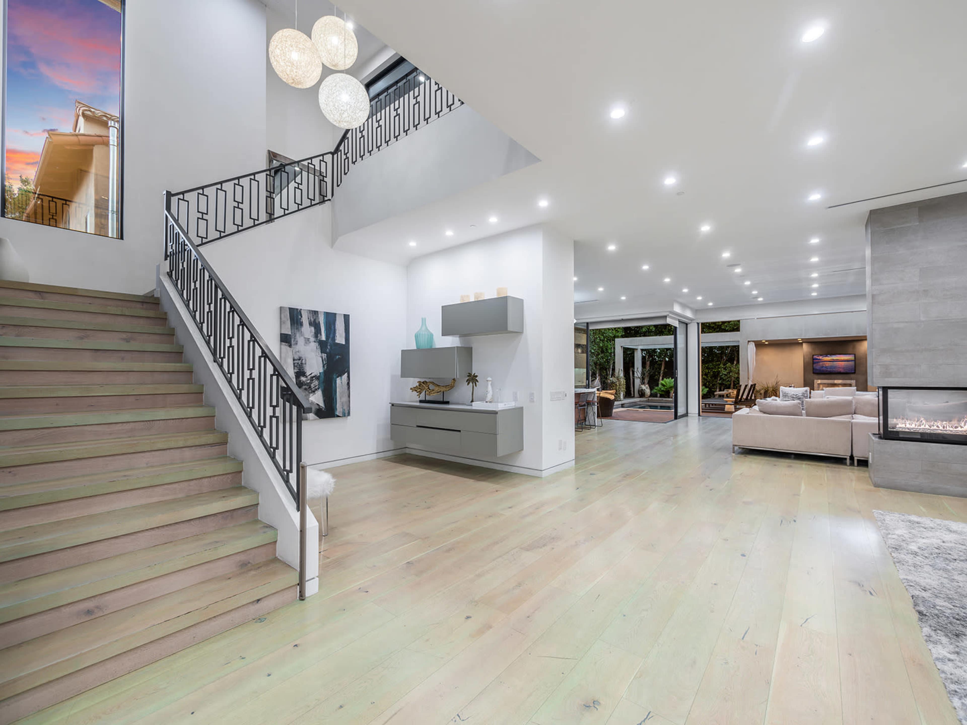 A modern interior features a staircase with decorative railing, an open living area, and large windows allowing natural light.
