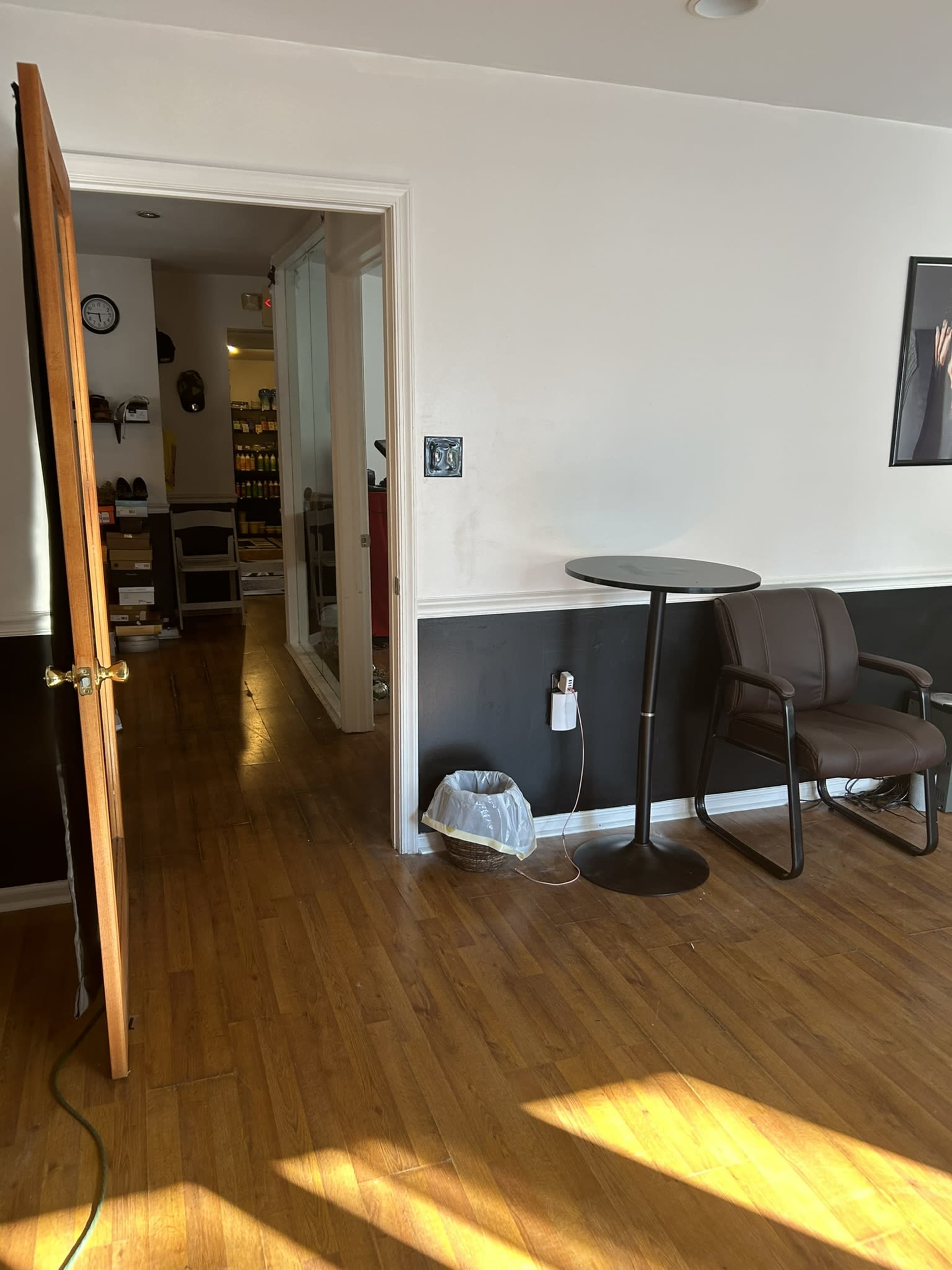 An open door reveals a small room with a table and chair, hardwood floors, and a hallway leading to another area.