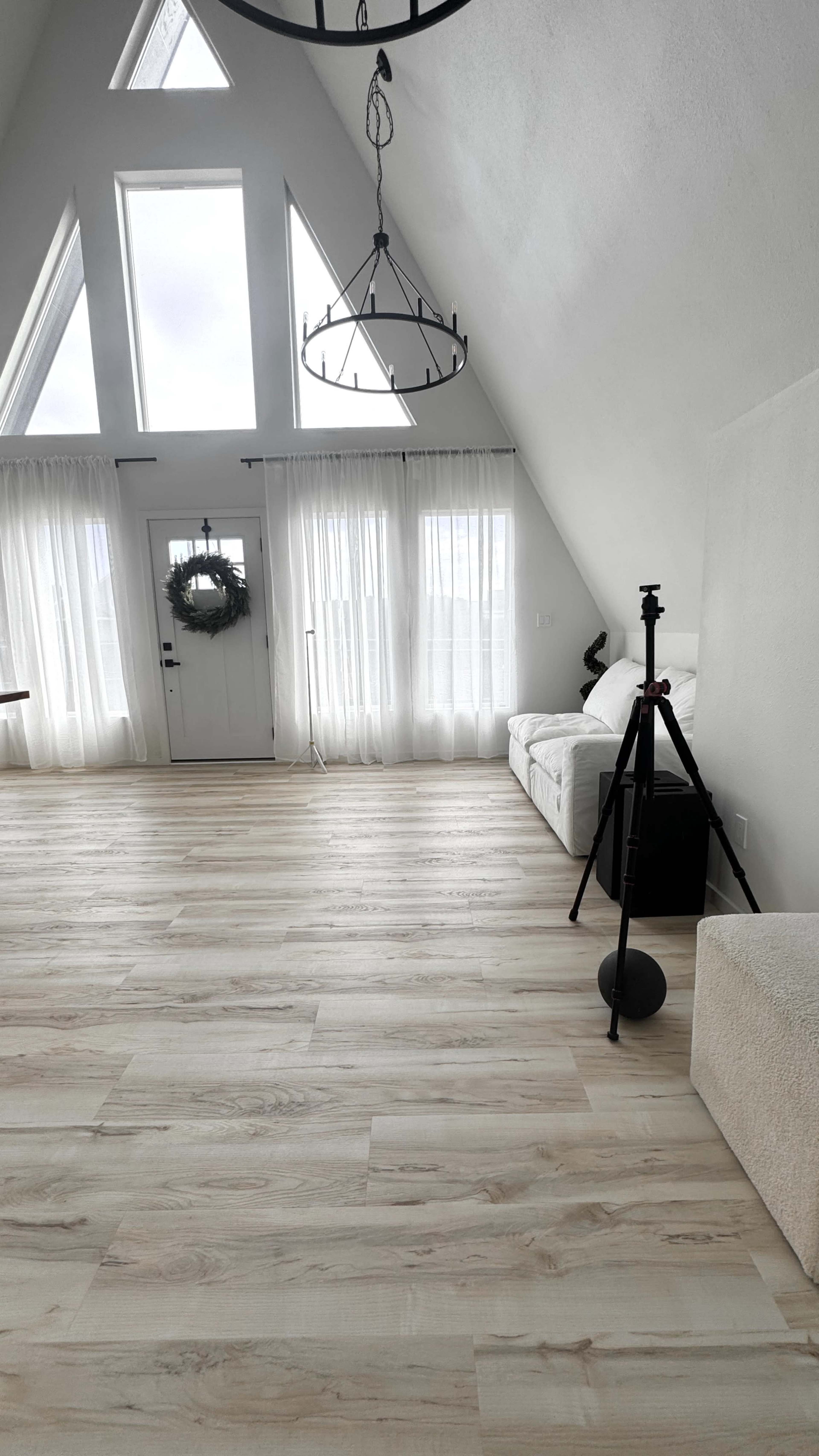 The image shows a bright, airy interior of a modern room with a high A-frame ceiling, large windows, and light wooden flooring.