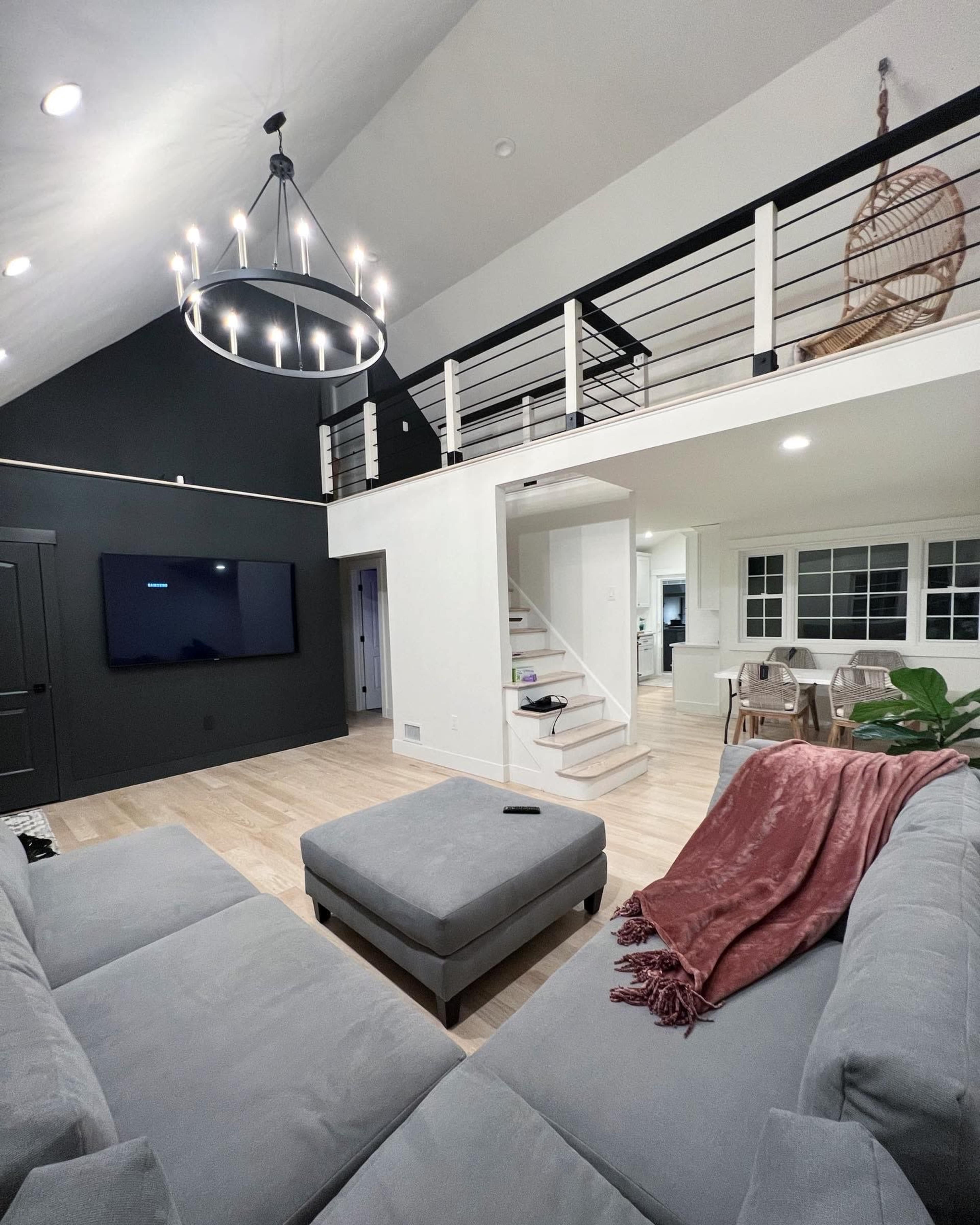 A modern living room features a gray sectional sofa, a large television mounted on the wall, and an open staircase leading to a lofted area.