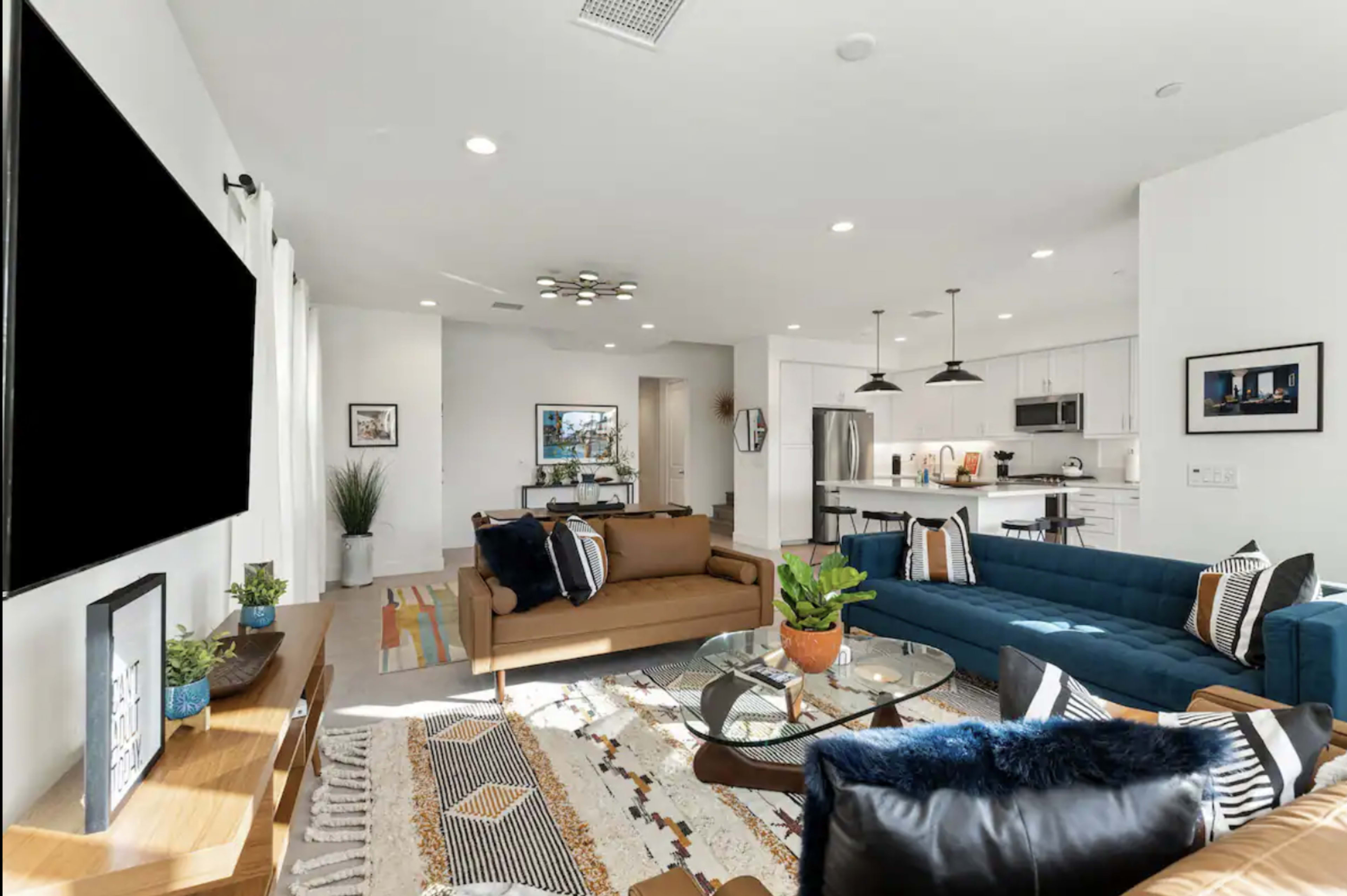 A modern living room with a blue sectional sofa, a brown couch, and a kitchen area visible in the background.