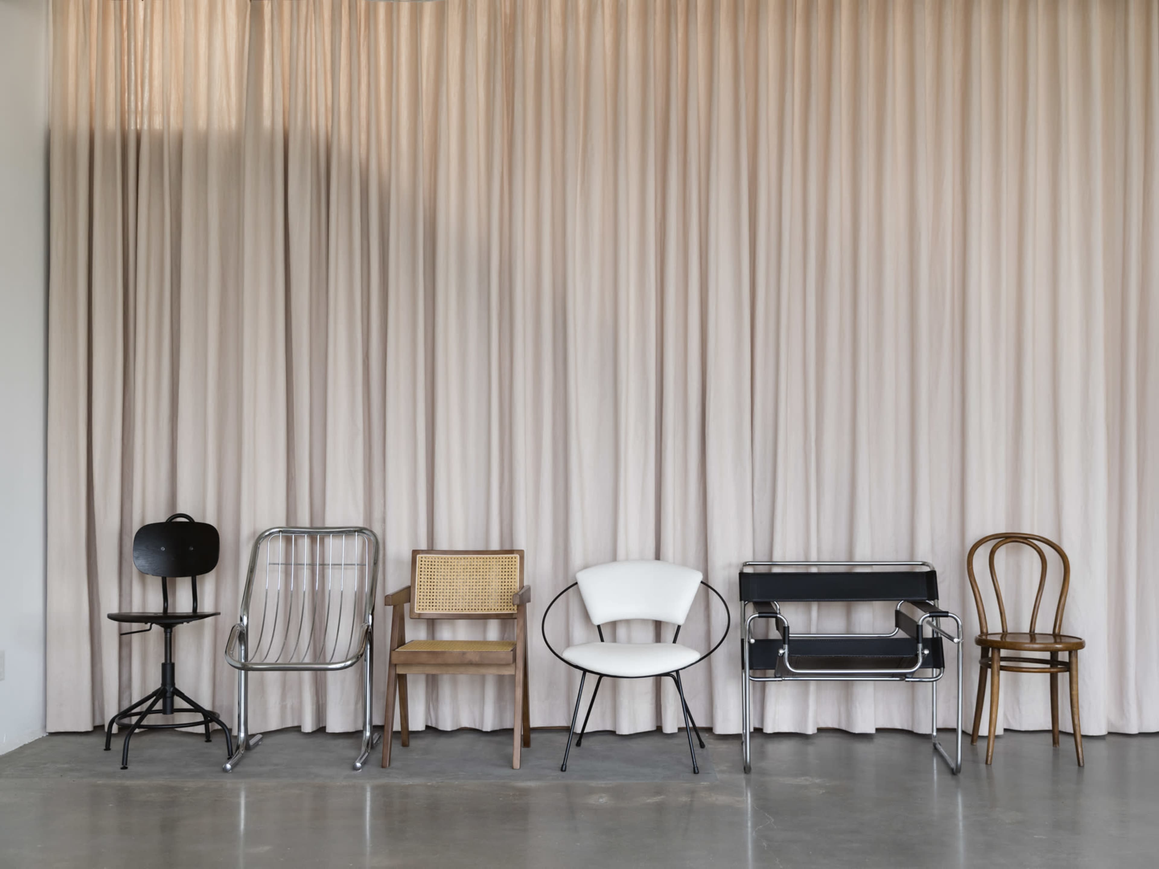 The image features a row of six distinct chairs against a backdrop of soft, light-colored curtains.