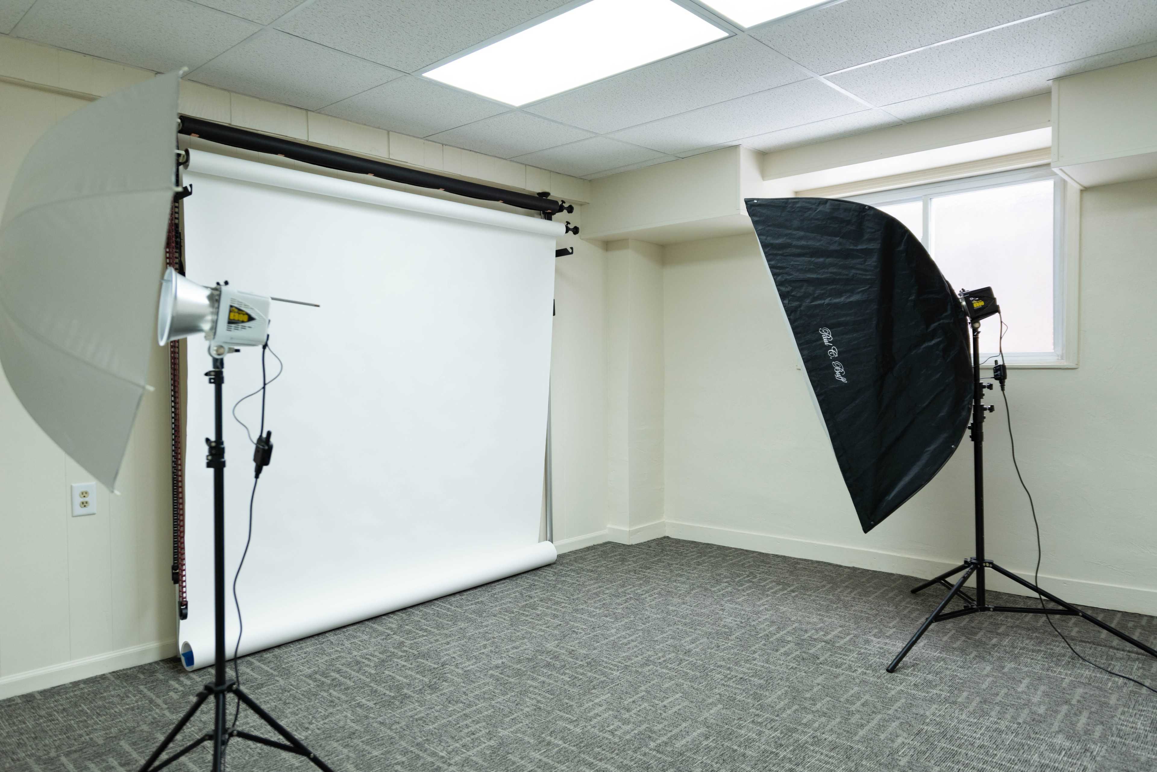 A photography studio setup with a white backdrop and two lighting umbrellas positioned on either side.