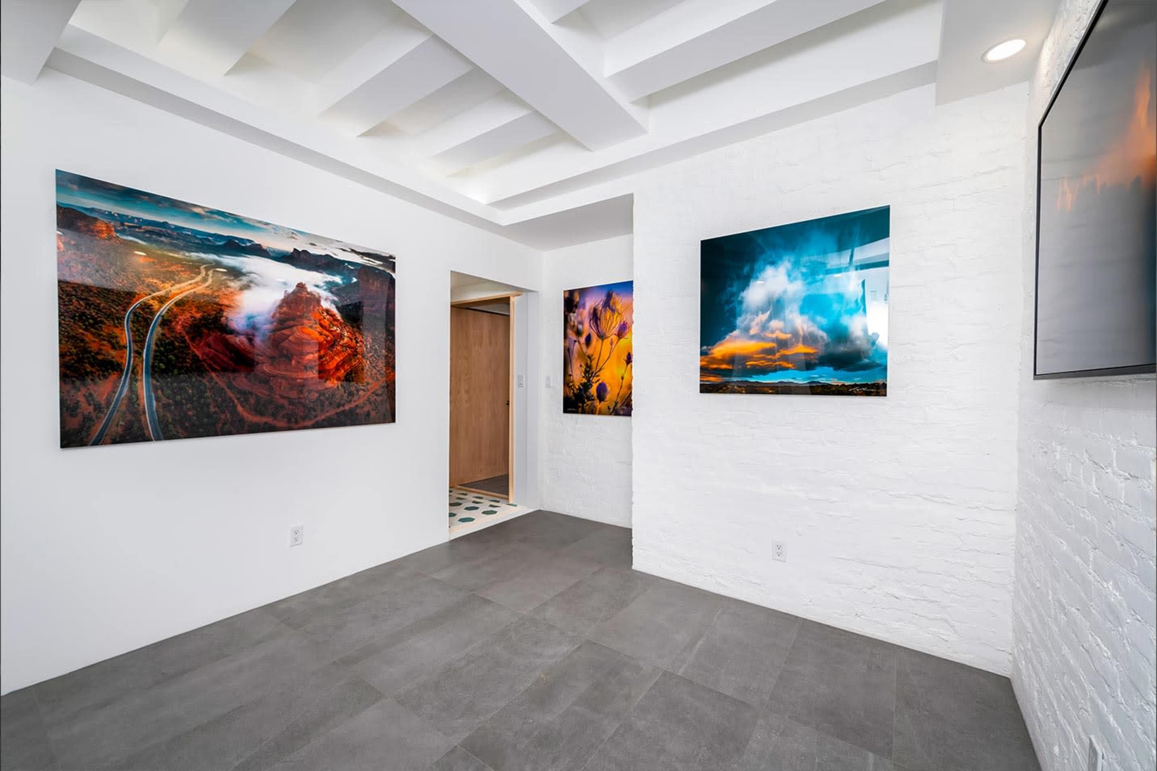 The image shows a gallery-like space with large landscape photographs displayed on the white walls, featuring a tiled entryway visible in the background.