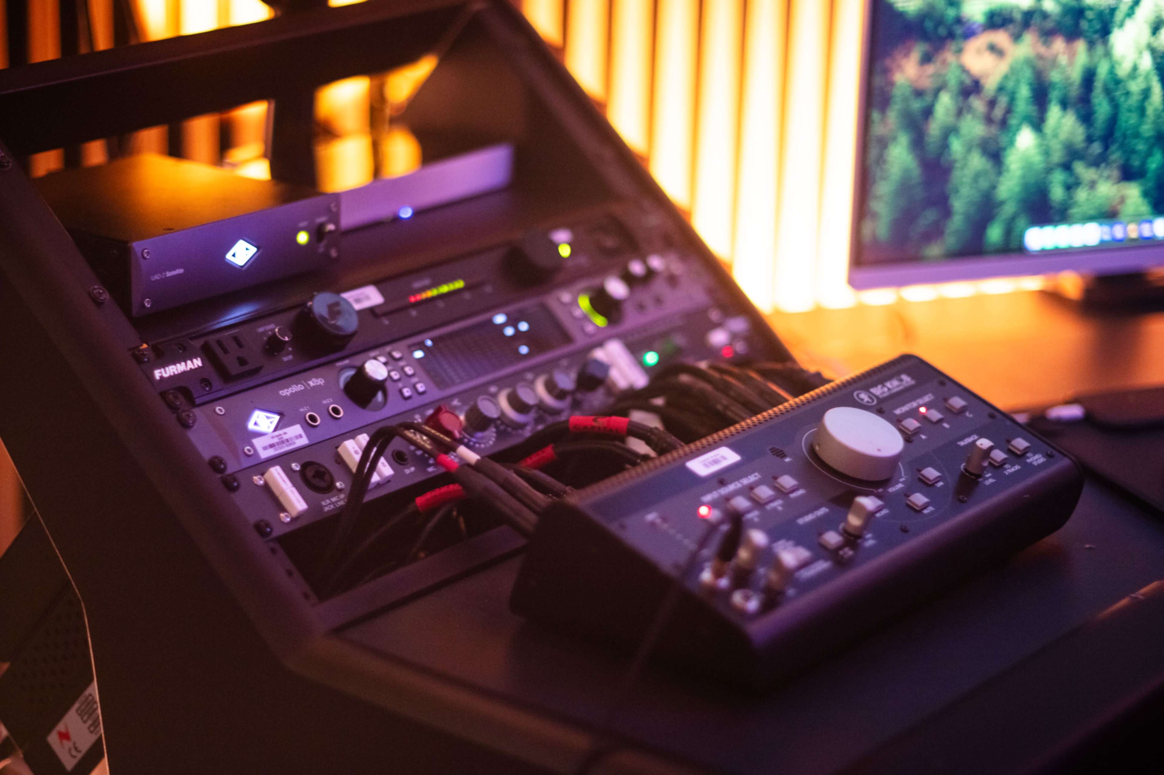 A rack-mounted audio equipment setup with various devices and connections, positioned next to a computer monitor.
