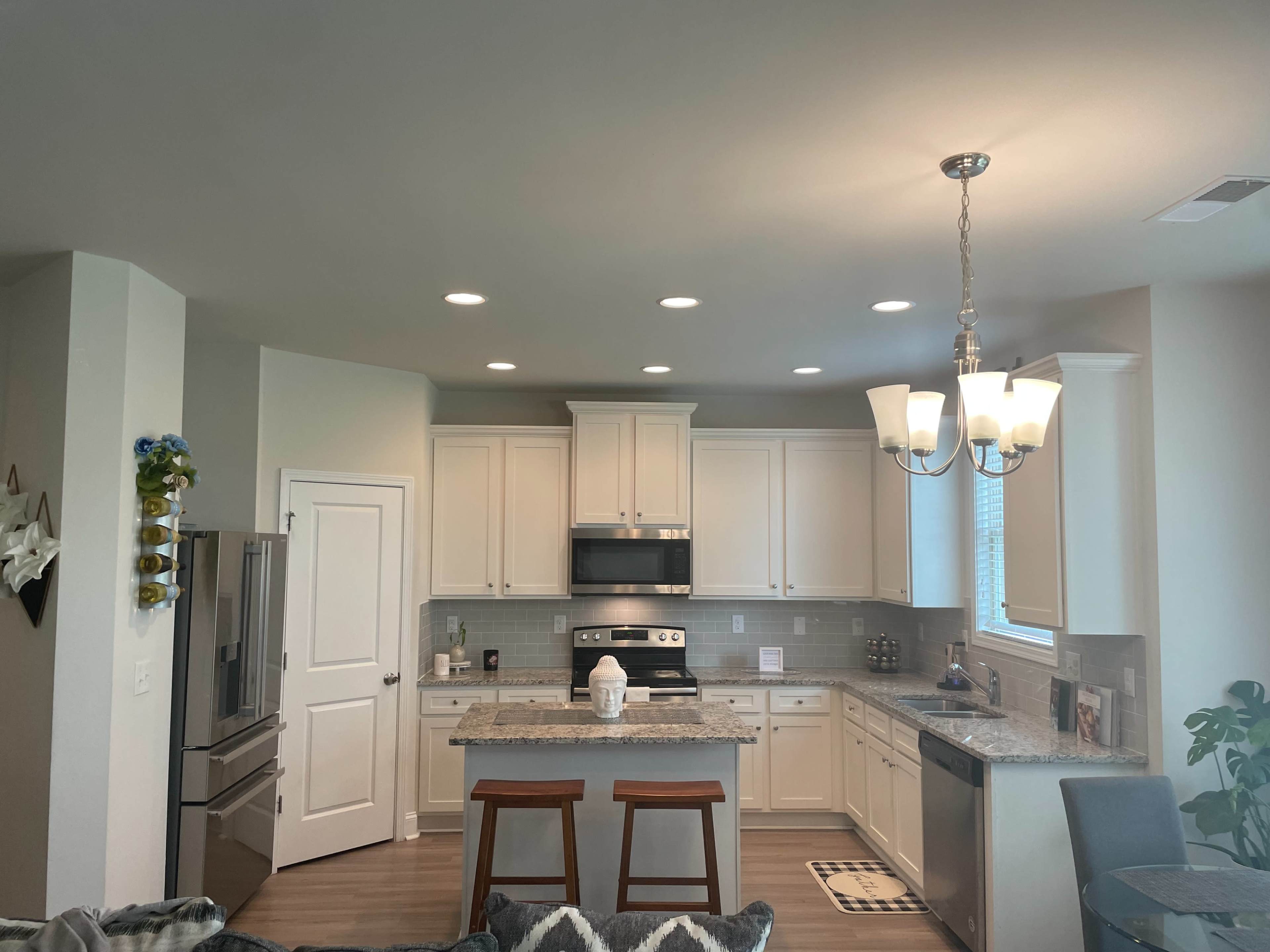 A modern kitchen features white cabinetry, stainless steel appliances, and a central island with two wooden bar stools.
