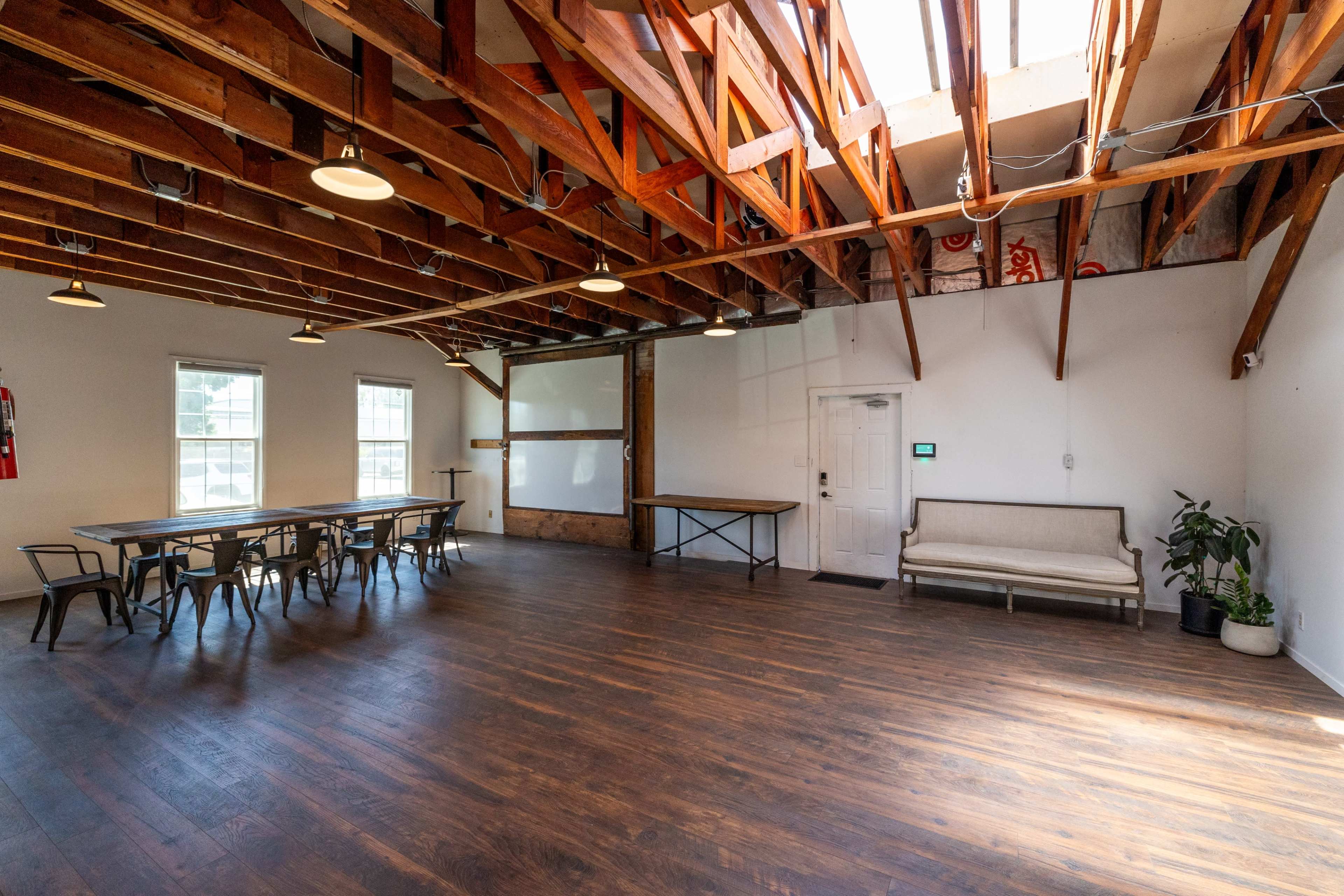 A spacious, bright room with wooden beams, a large table set for meetings, and a couch in one corner.