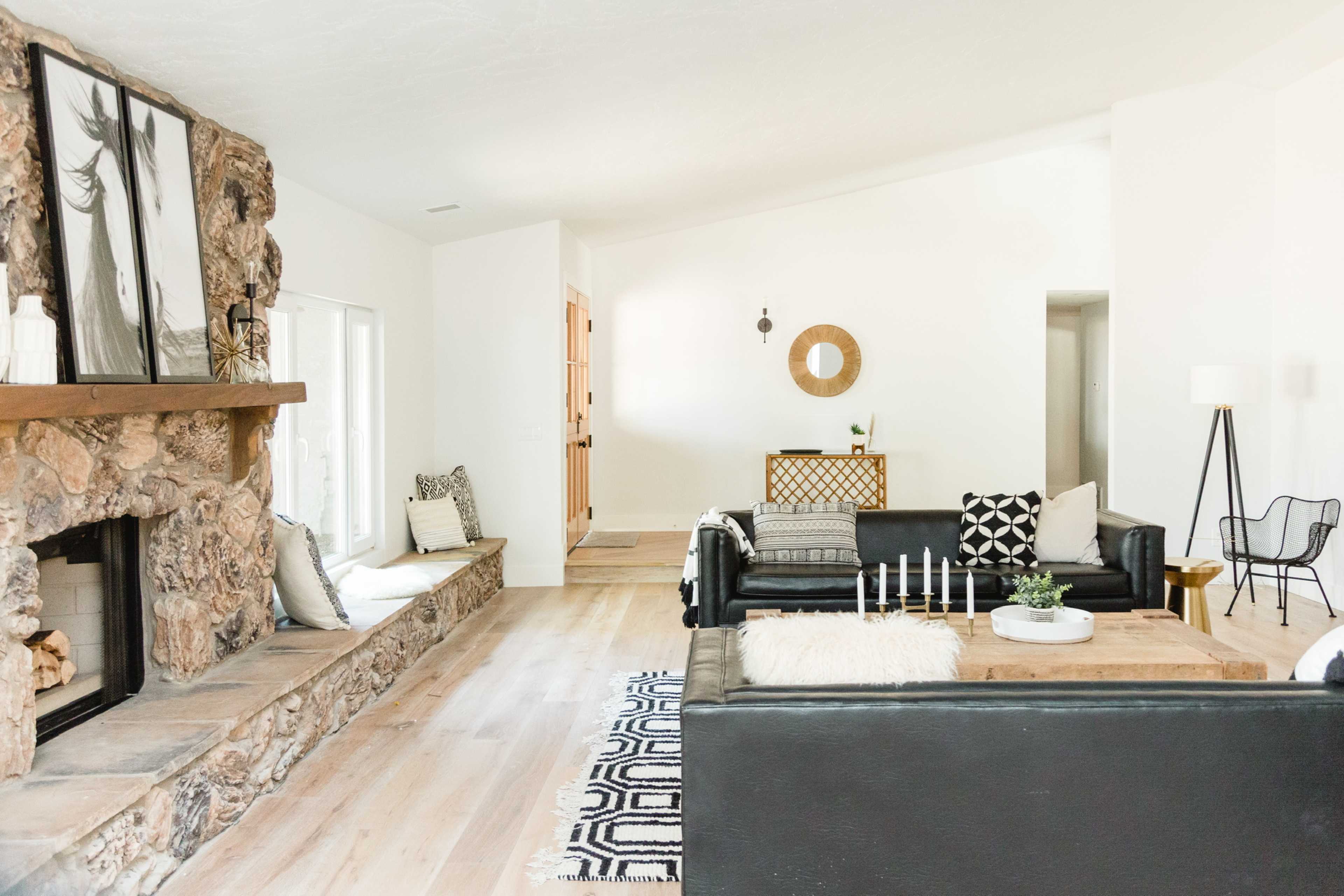 A modern living room features a stone fireplace, black leather sofas, a wooden coffee table, and stylish decor against light-colored walls.