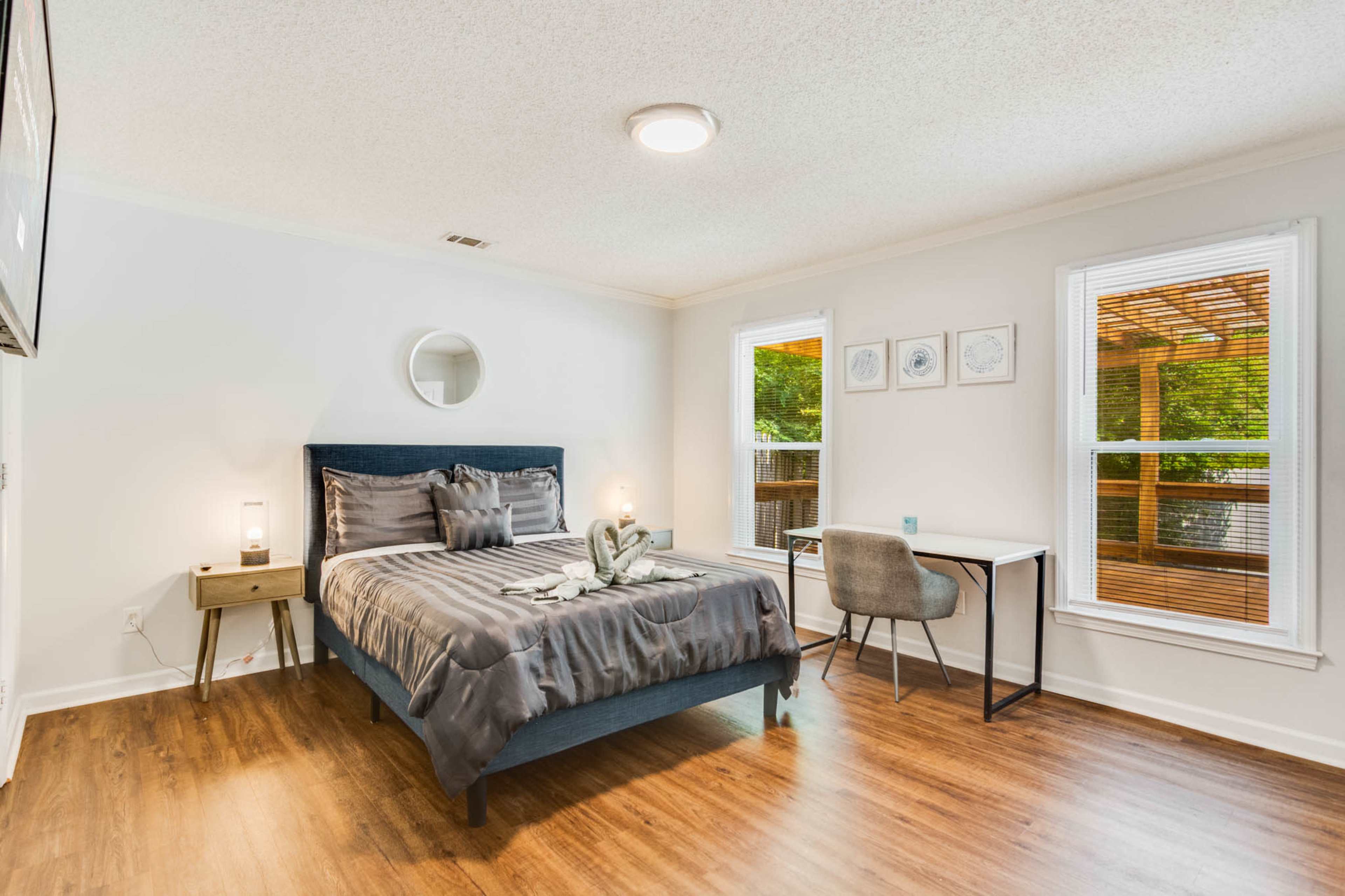 The image shows a bedroom with a bed, a side table, and a small desk by the window.