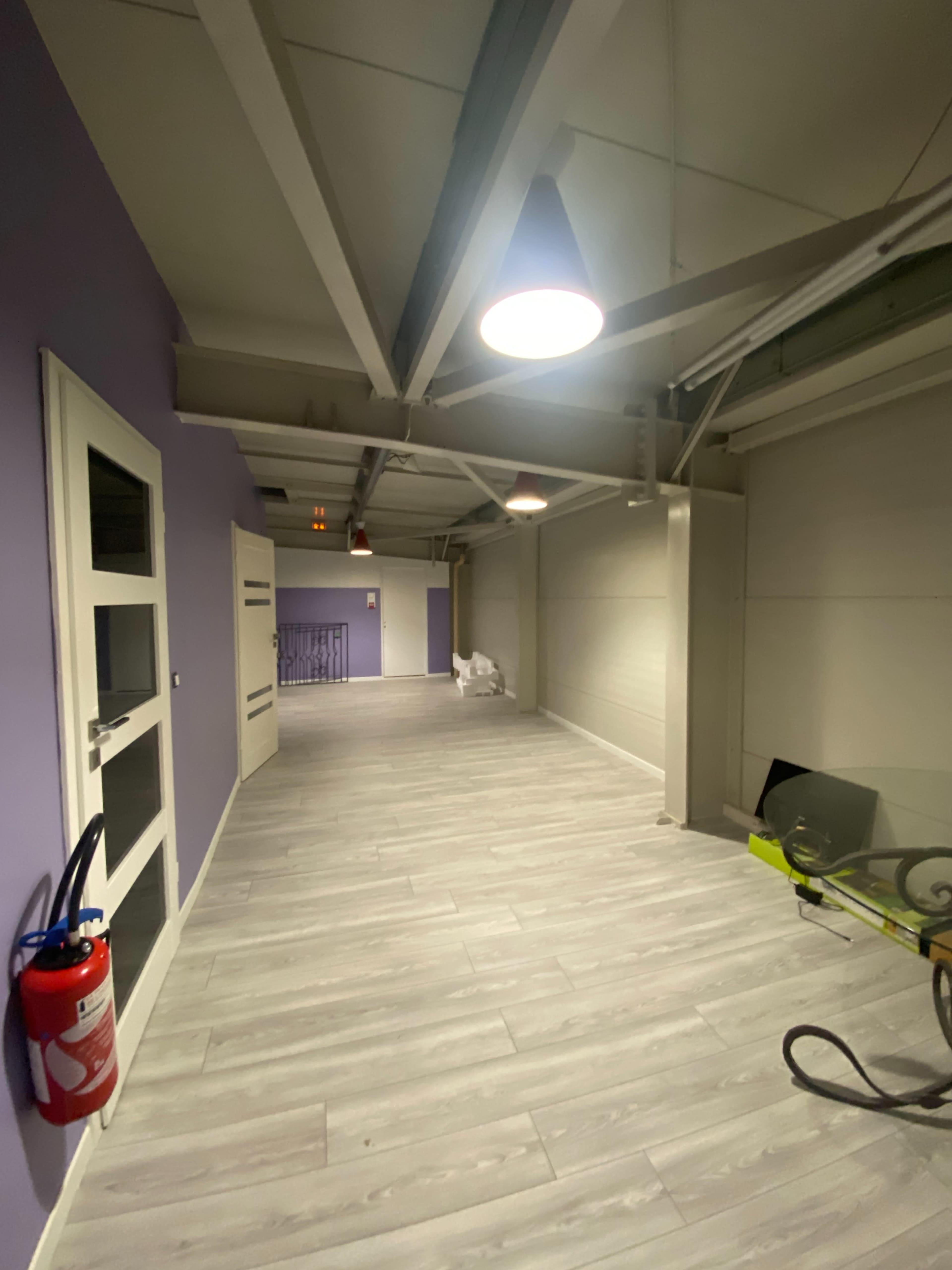 The image shows a corridor with purple walls, overhead lighting, and tiled flooring, featuring a fire extinguisher on the left side.