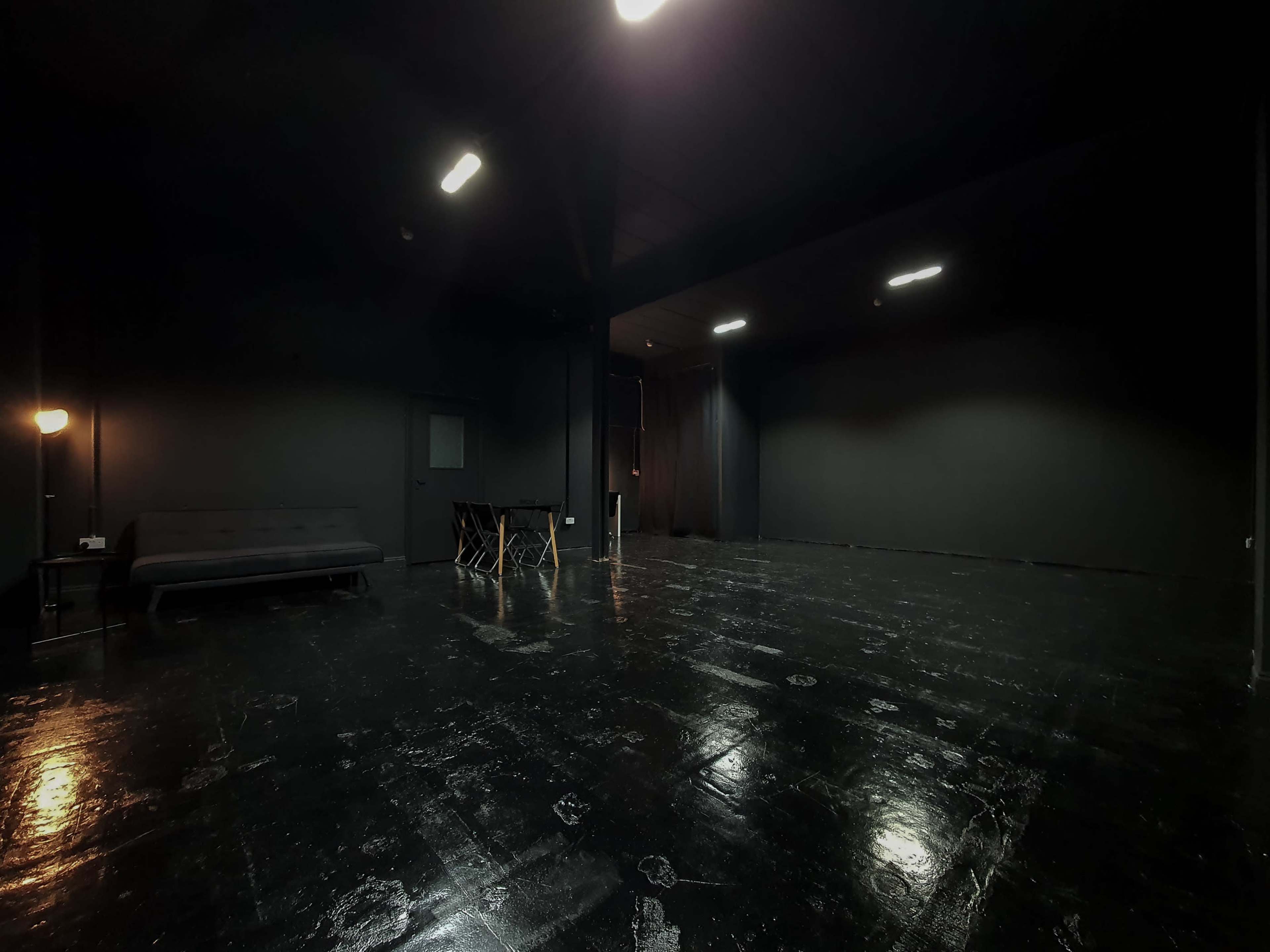 A dimly lit black room with a sofa, a table with chairs, and a curtained exit.