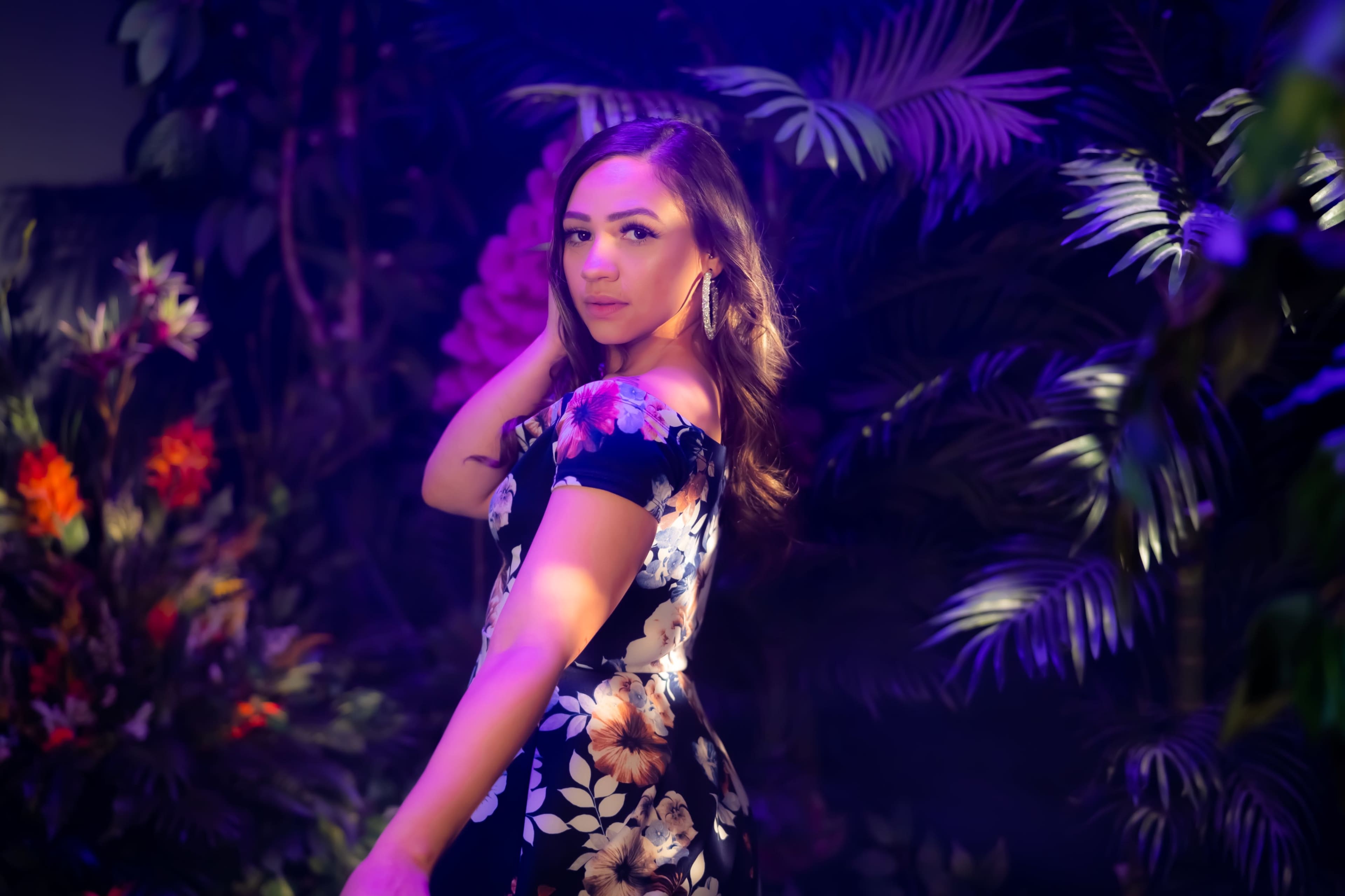A woman poses in a floral dress against a backdrop of lush tropical plants.