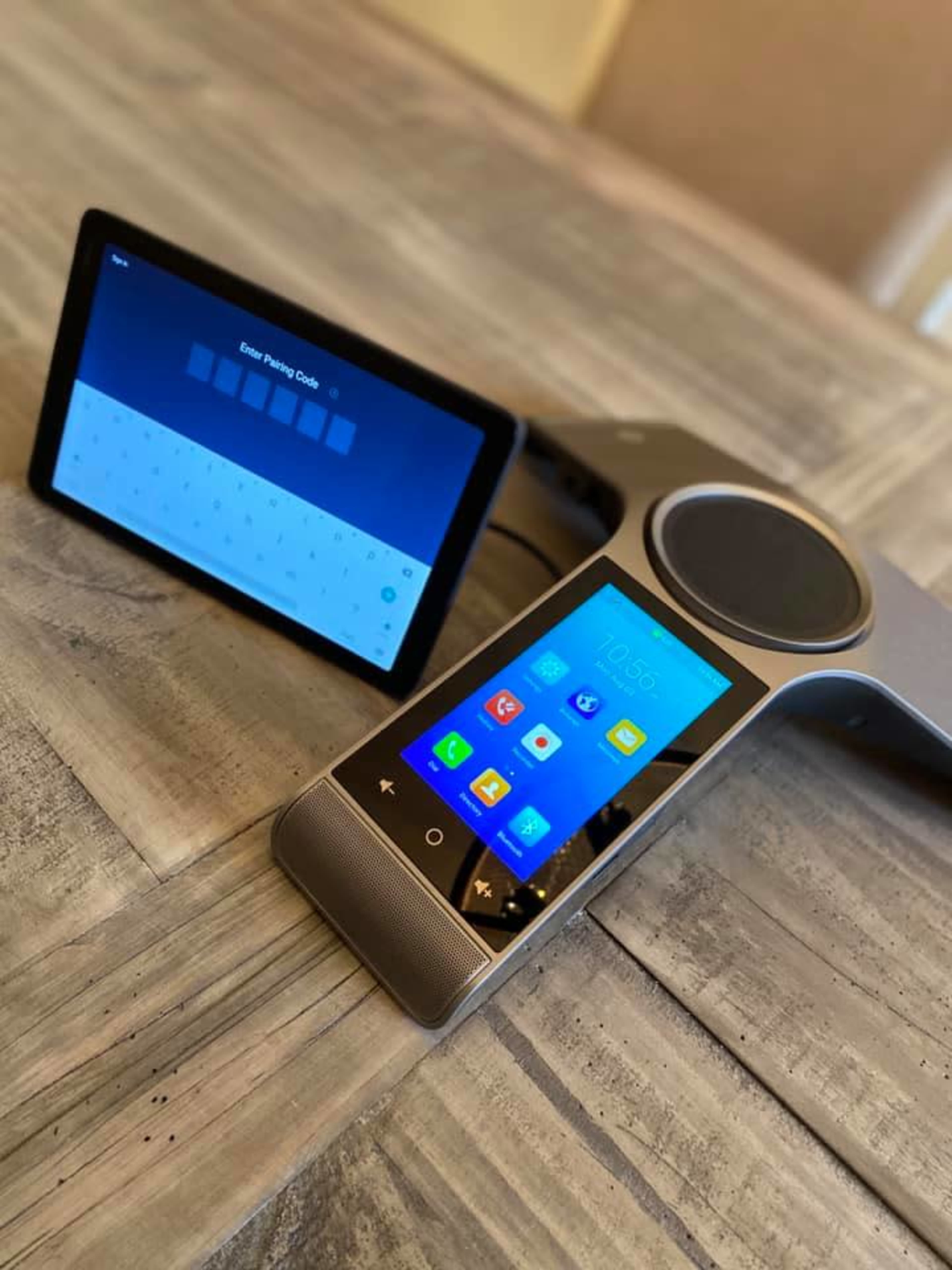 A touchscreen device with a circular speaker and a separate tablet displaying a password input screen, all placed on a wooden table.