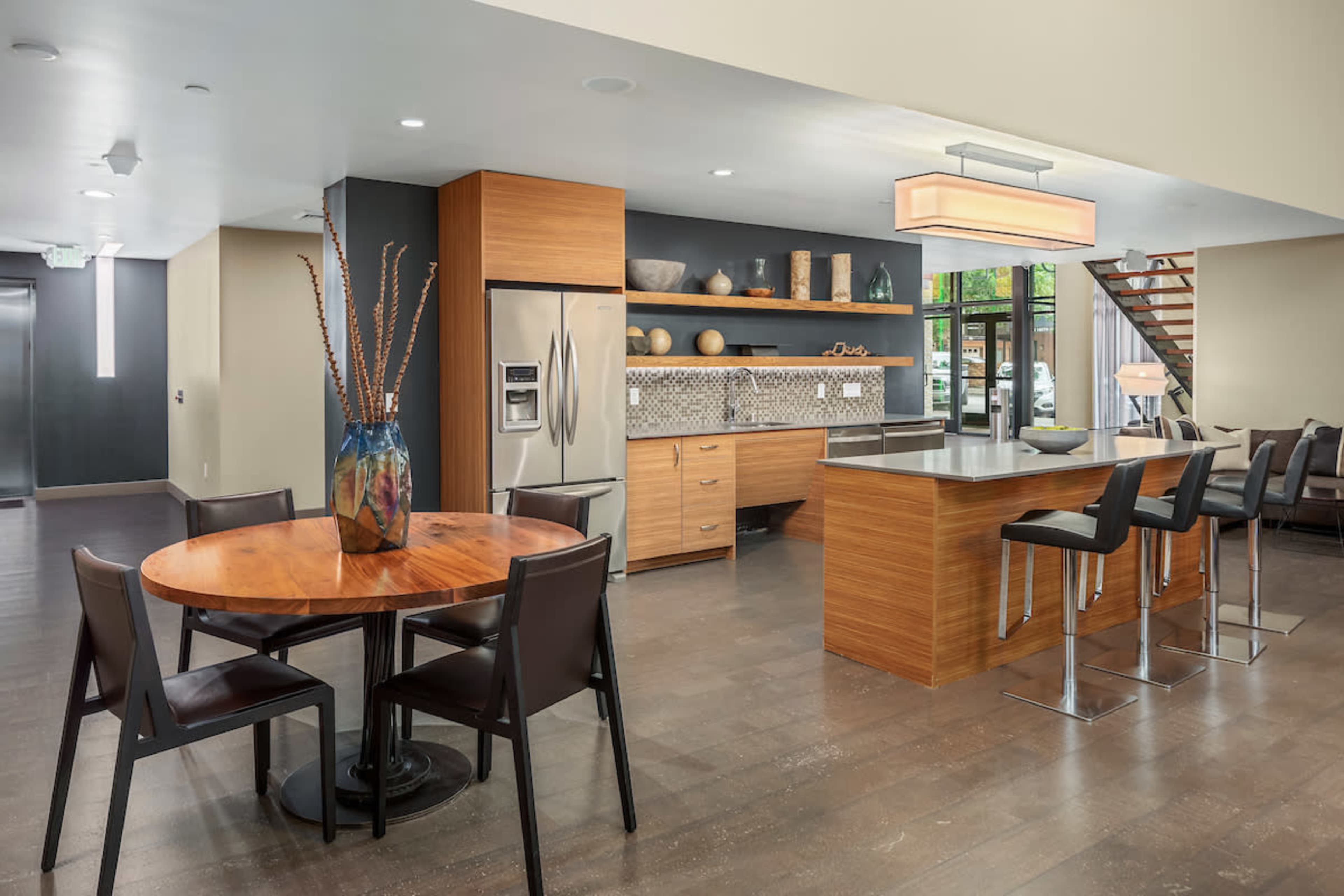 A modern kitchen and dining area featuring a round wooden table, black chairs, a stainless steel refrigerator, and a sleek kitchen island with bar stools.