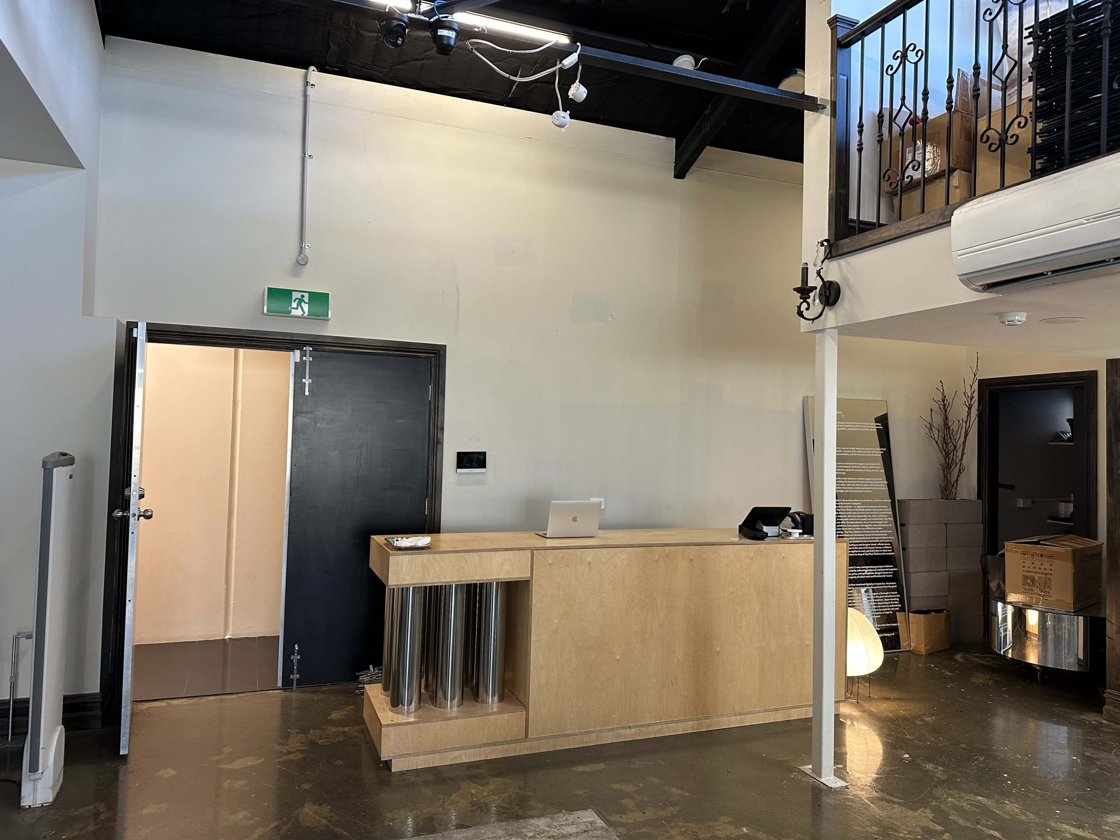 The image shows a modern reception area with a wooden front desk, a door to the left, and a staircase leading to an upper level.
