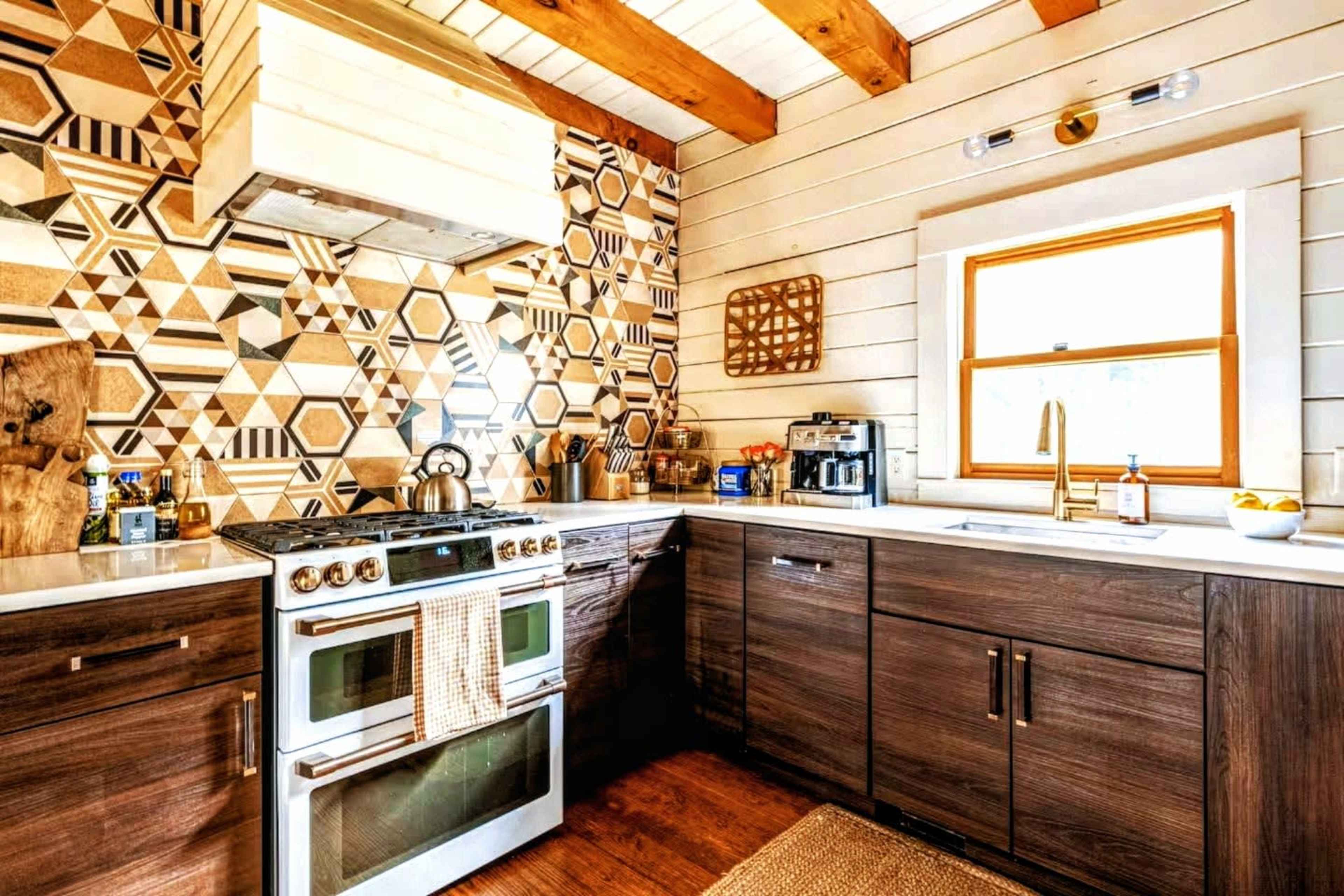The kitchen features a modern design with a geometric patterned backsplash, wooden beams, and stainless steel appliances.