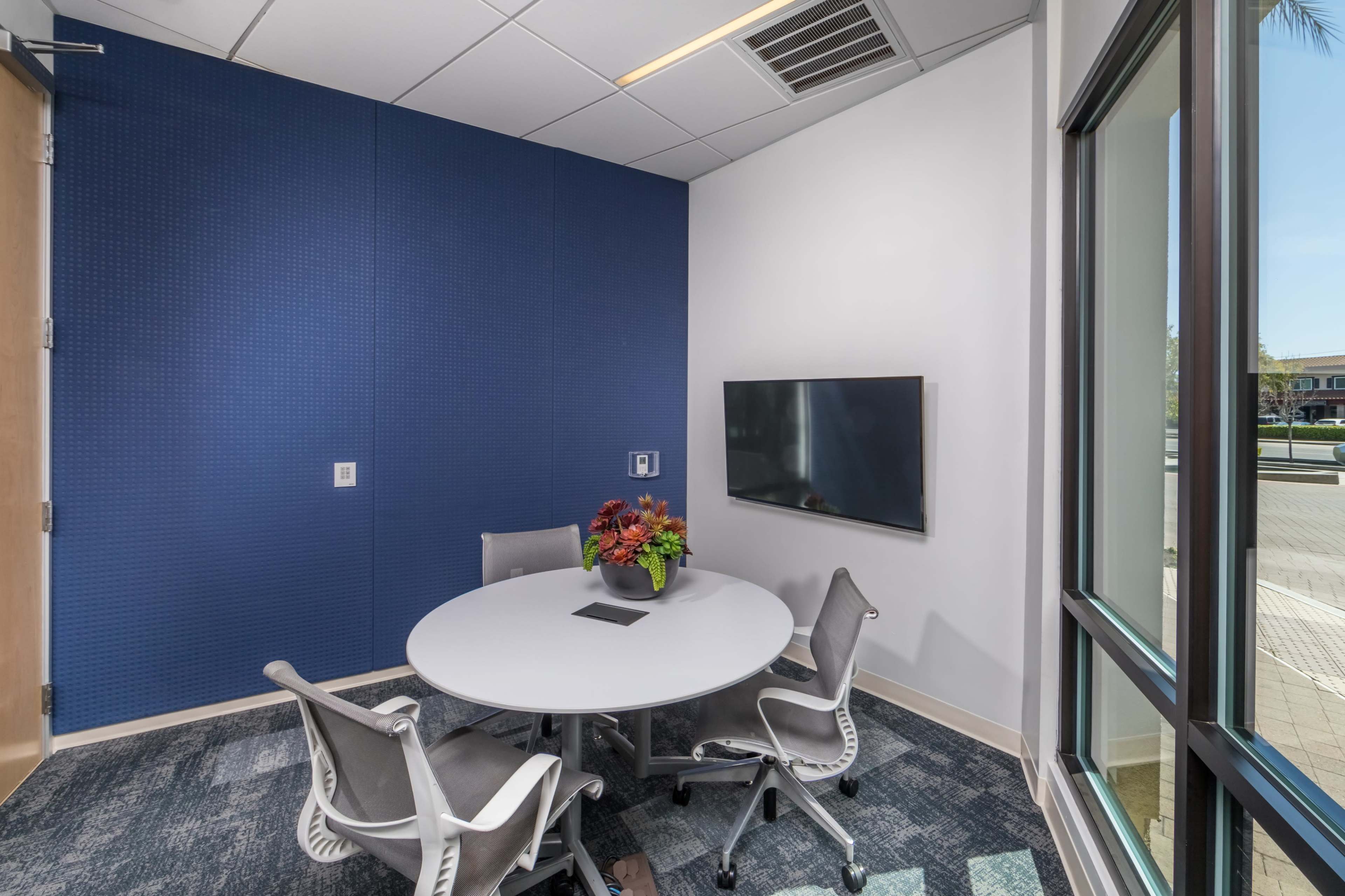 A small conference room features a round table with four chairs and a wall-mounted television.