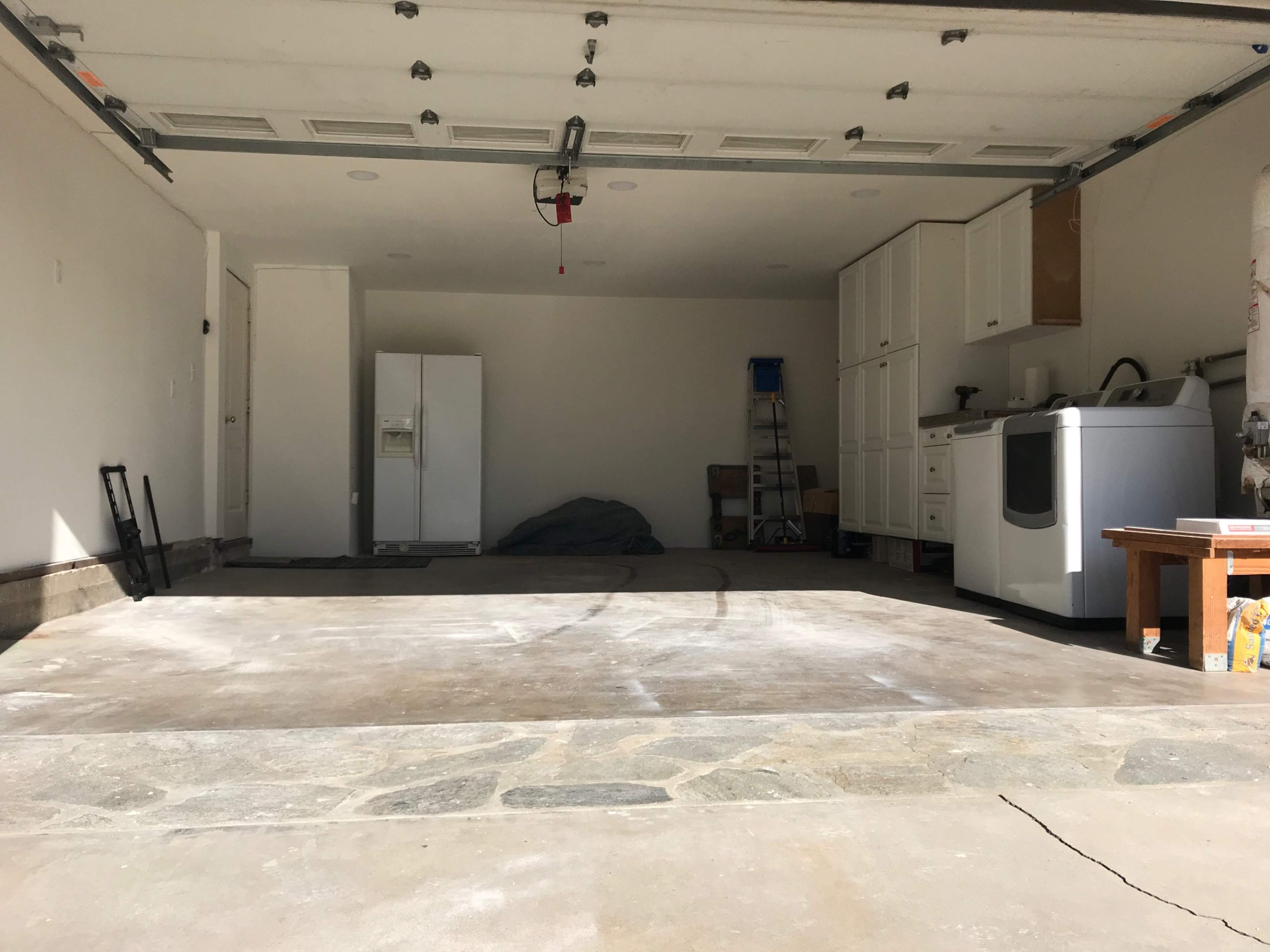 An empty garage with a refrigerator, a washing machine, and storage cabinets along one wall.