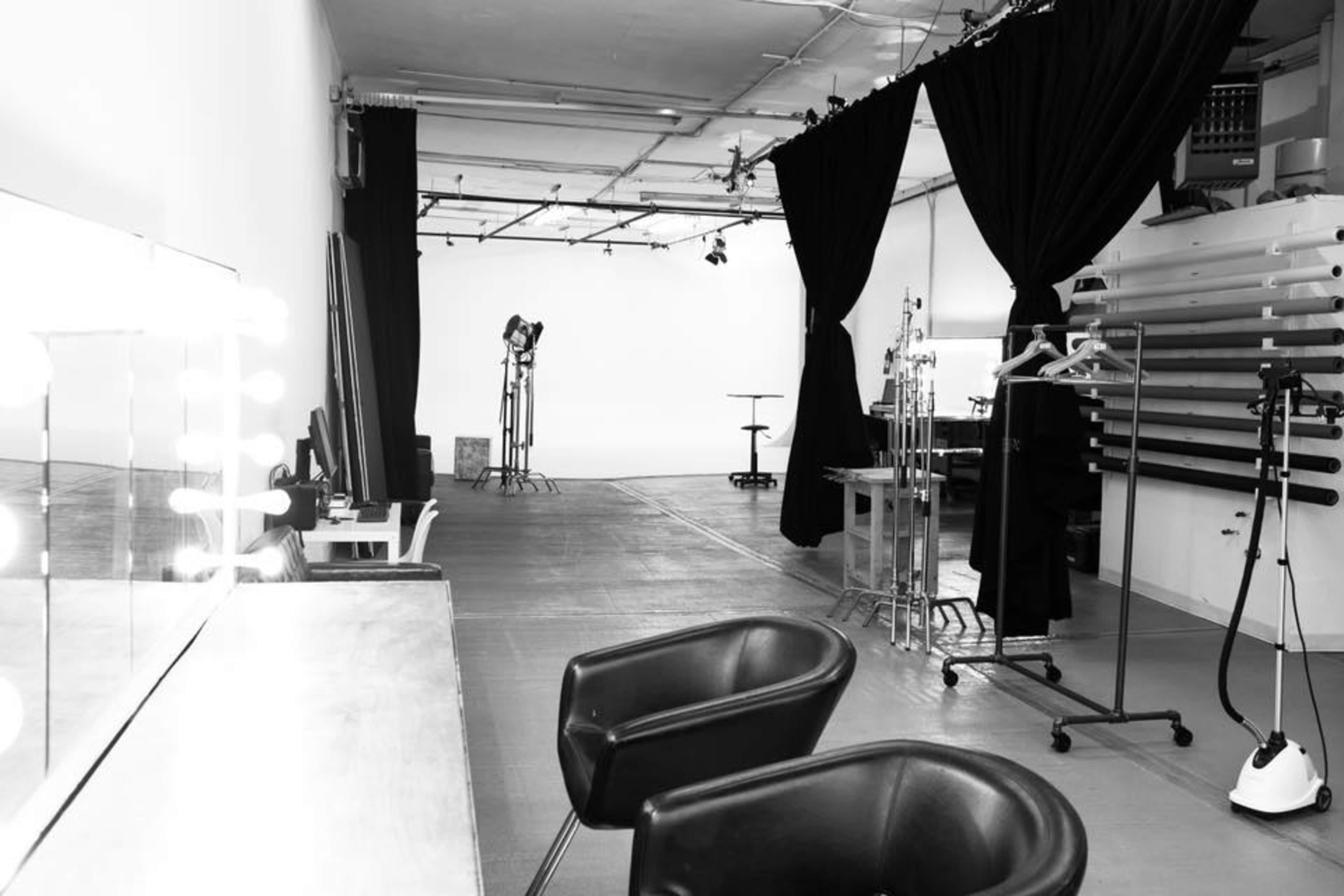 A spacious, minimally furnished studio with black curtains, makeup stations, and lighting equipment.