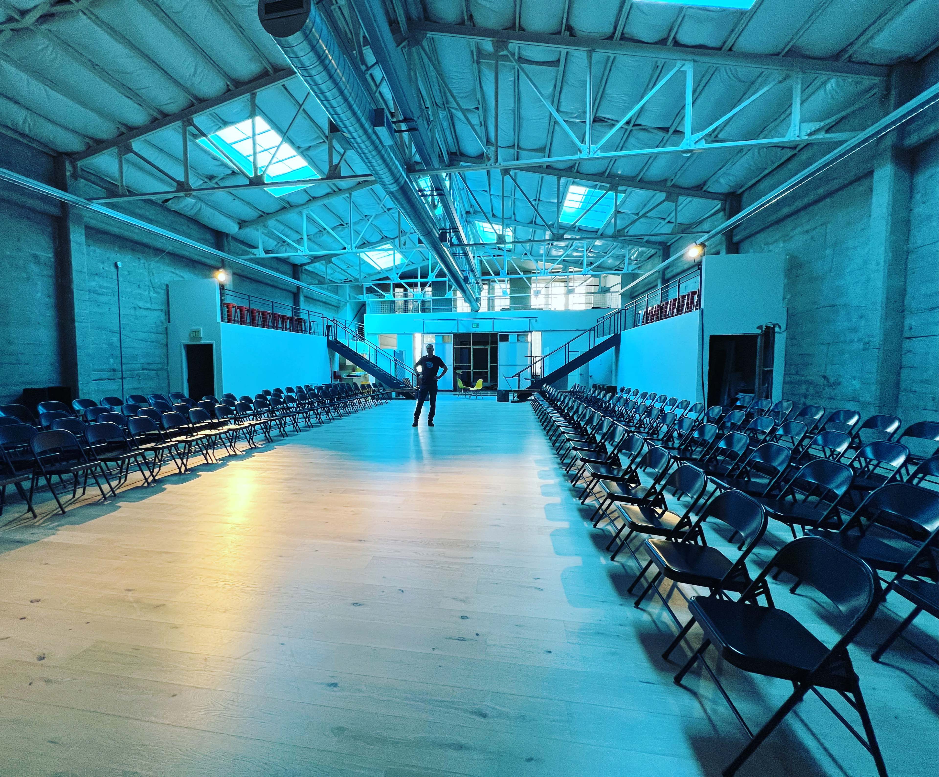 A long, narrow room with rows of black chairs on either side and a figure standing in the center.