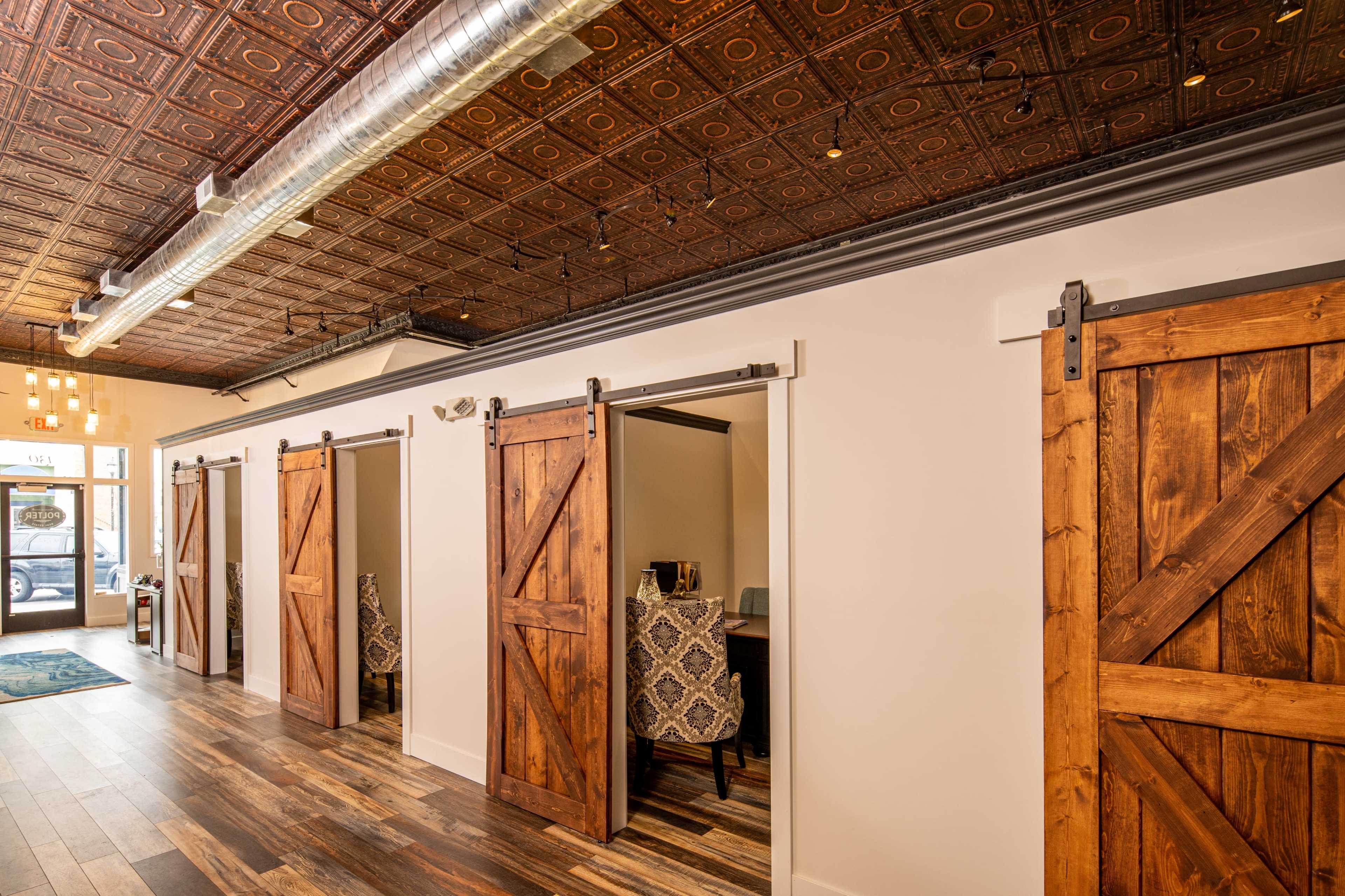 A corridor with several wooden sliding doors leading to private rooms, under a tin ceiling and with hardwood flooring.