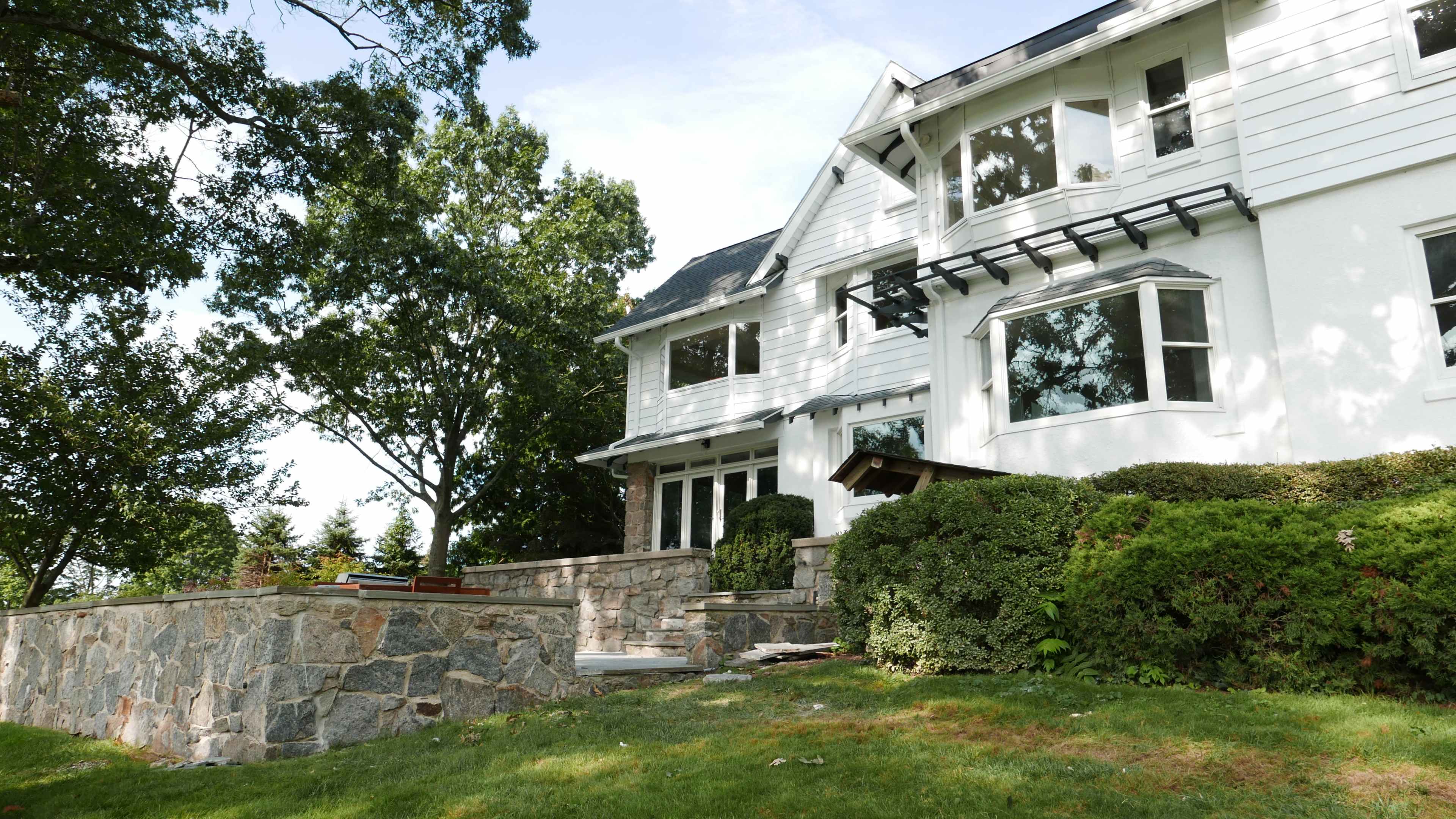 A multi-story house with white siding and stone accents is set on a landscaped yard with green grass and trees.