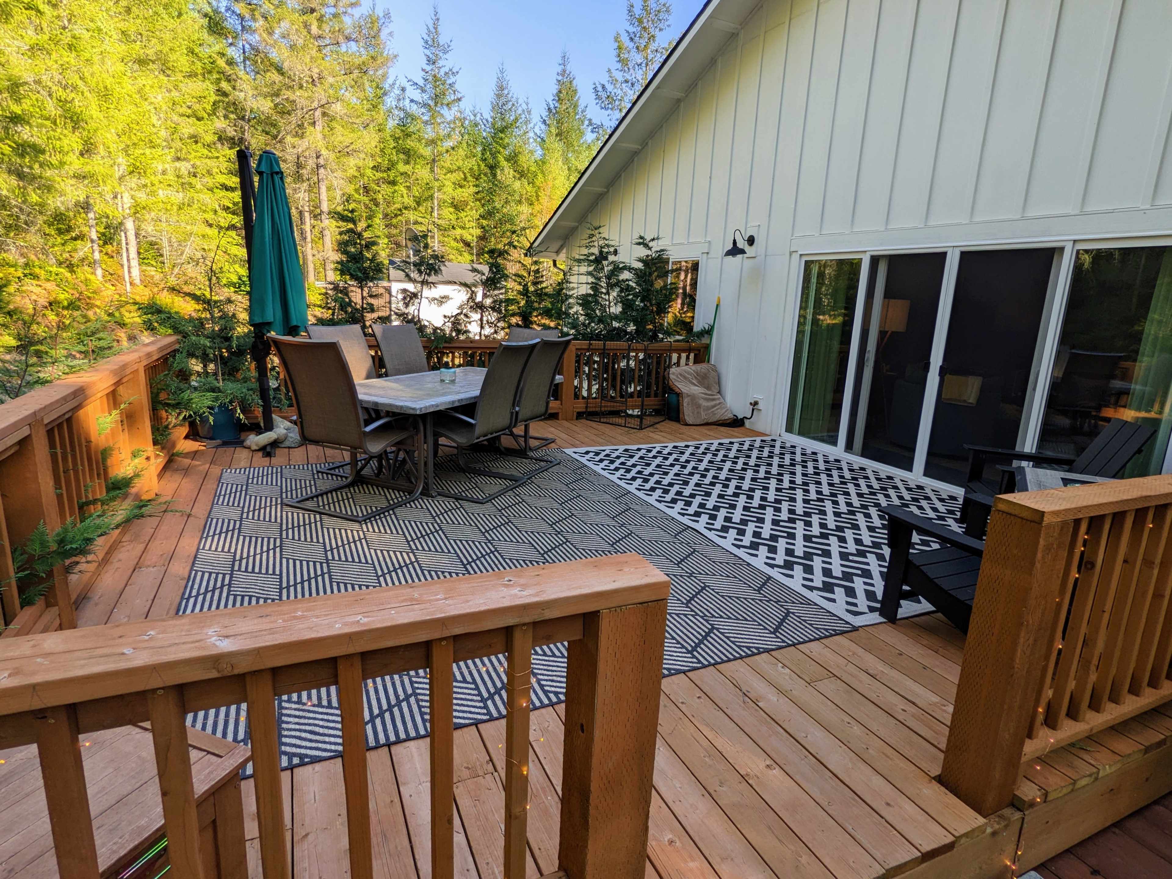 A wooden deck with patio furniture and a large outdoor rug, surrounded by trees.